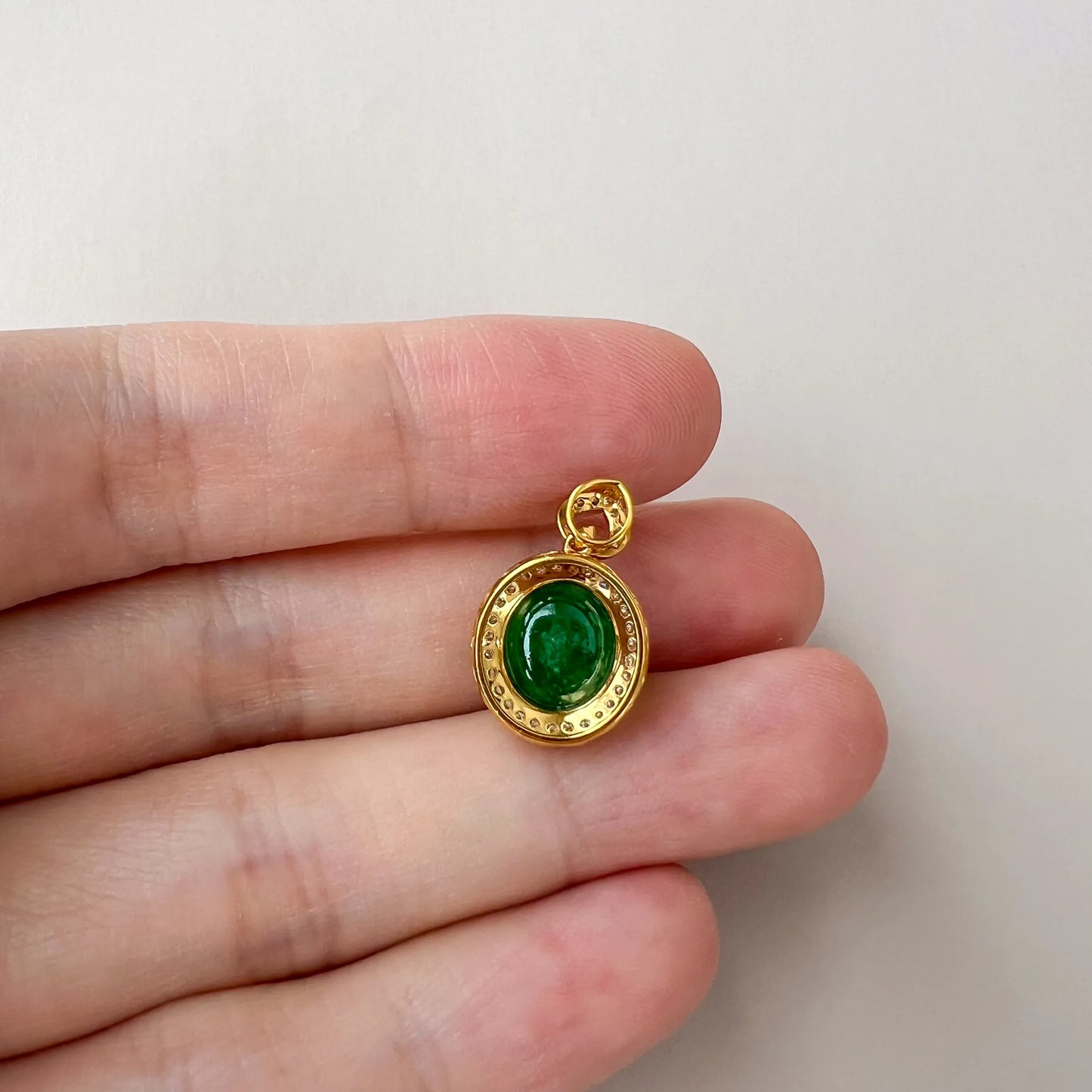 Close-up of green oval jade cabochon pendant with polished gold-tone bezel, beaded rim, and open bail