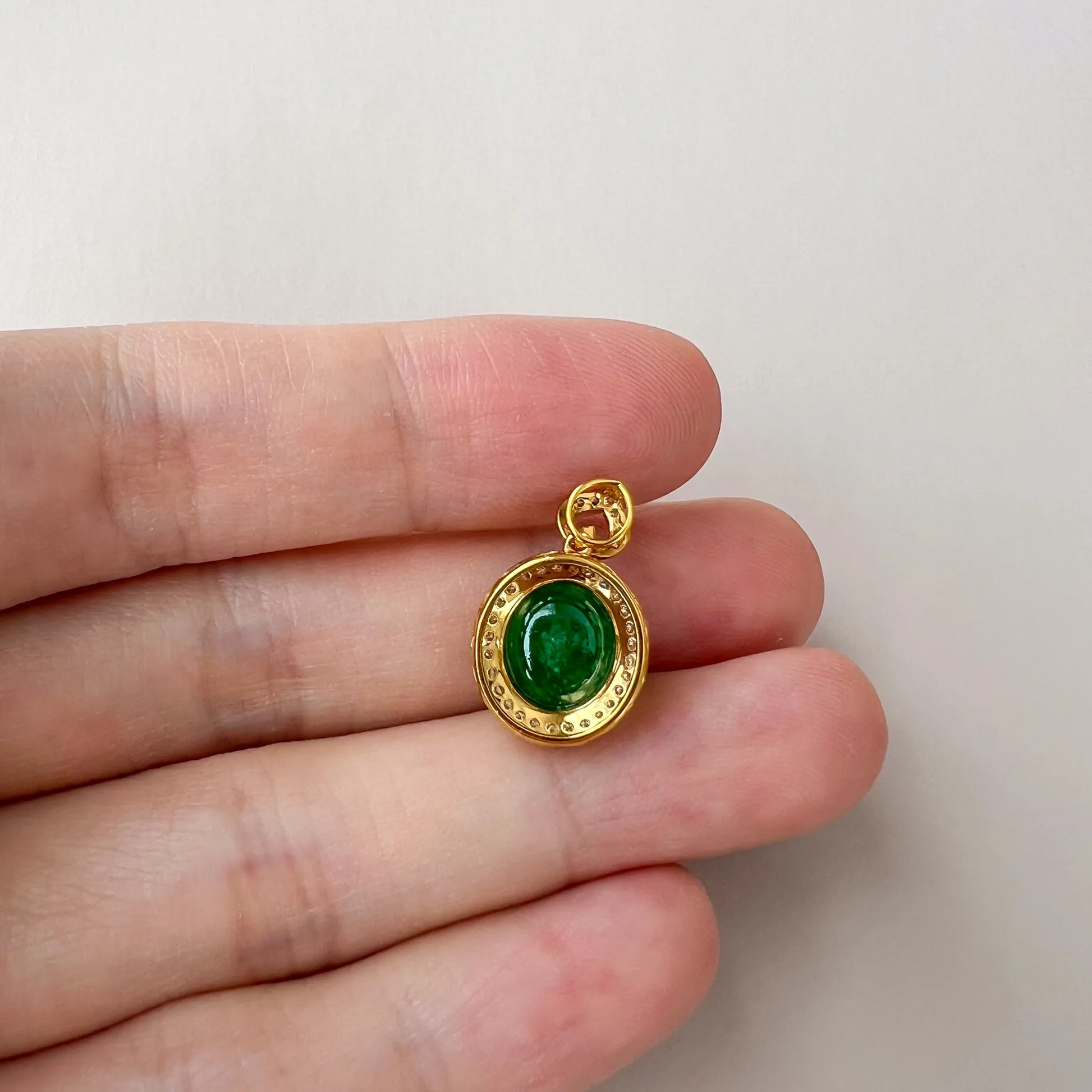 Close-up of green oval jade cabochon pendant with polished gold-tone bezel, beaded rim, and open bail
