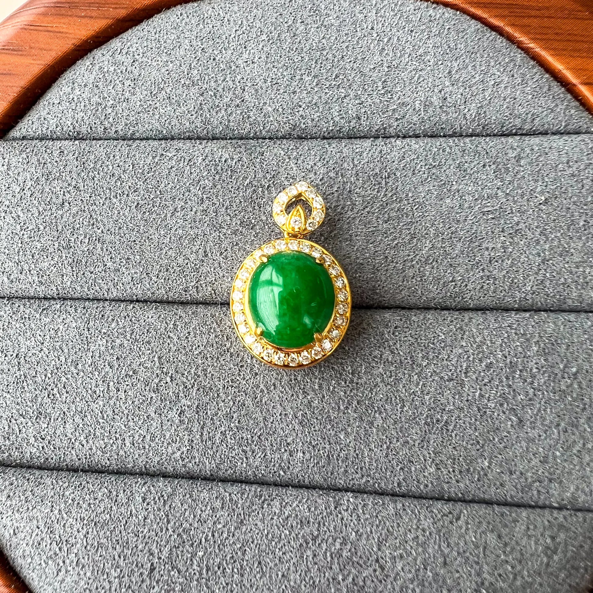 Front-facing pendant on gray jewelry tray, oval green cabochon with gold and diamond accents