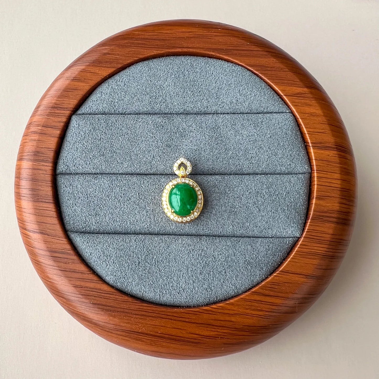 Pendant displayed in round wooden jewelry box, green cabochon stone in gold halo setting