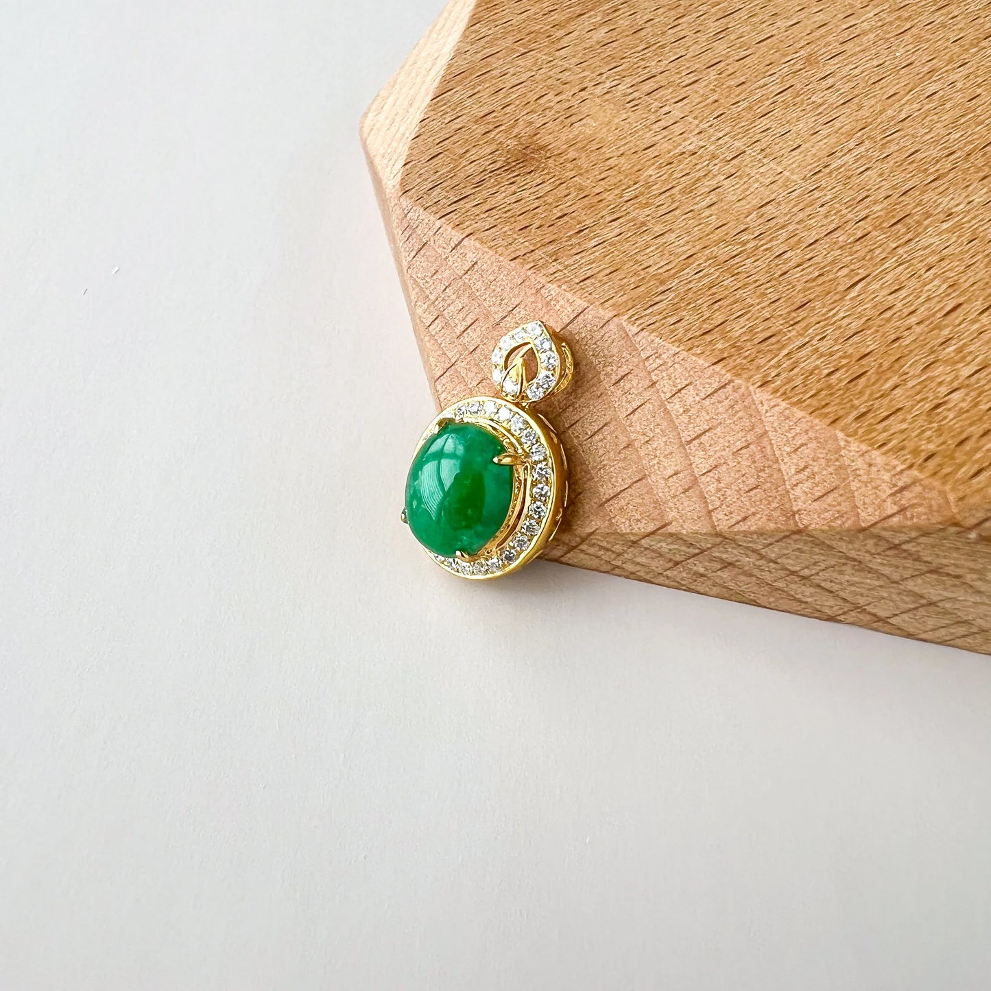 Angled side view of gold pendant with oval green stone and diamond halo on wood surface