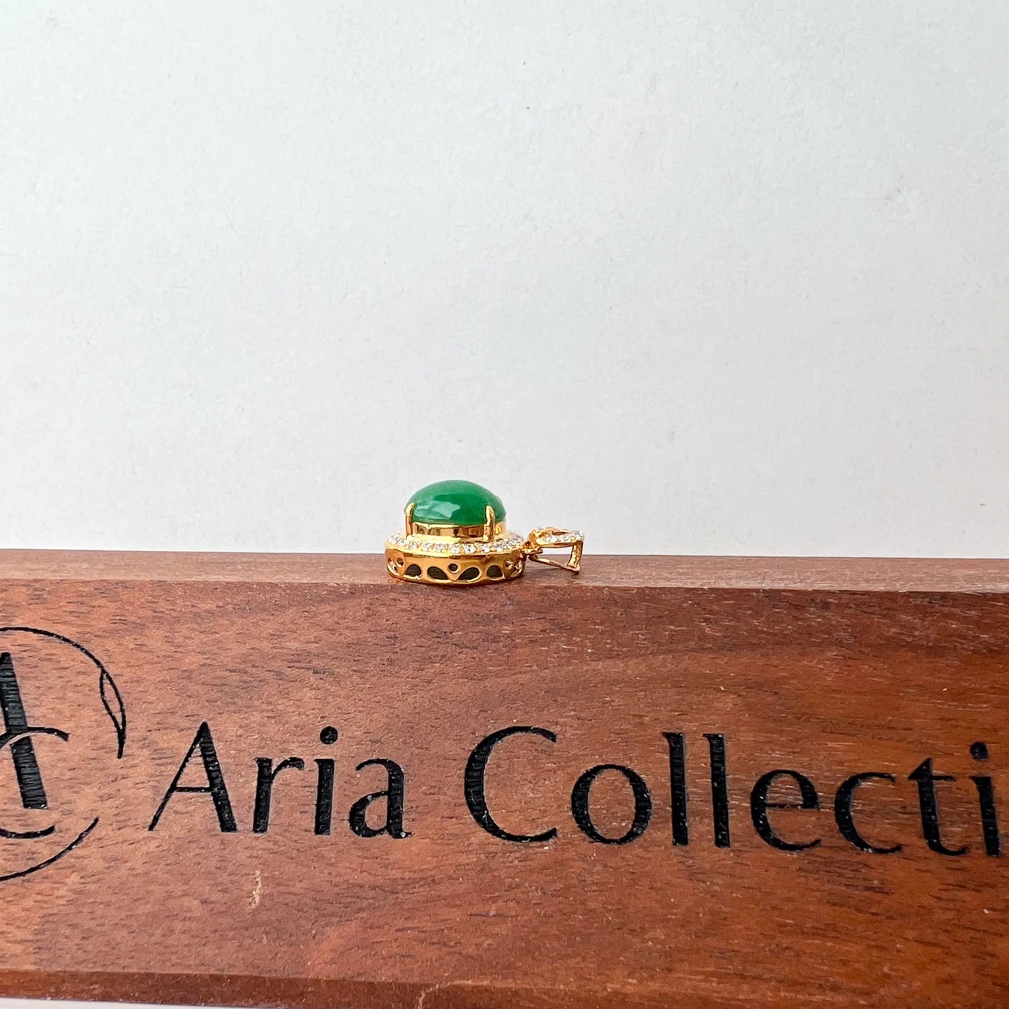 Side profile of gold pendant showing raised green cabochon and openwork gallery on wood