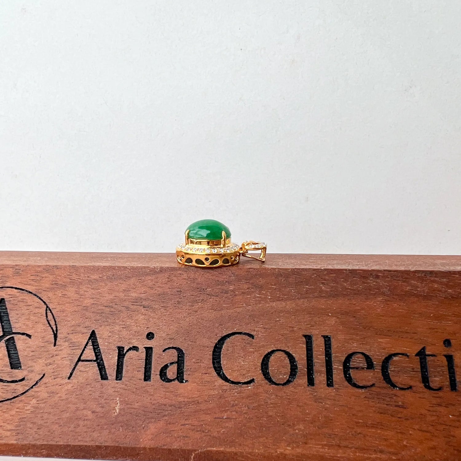 Side profile of gold pendant showing raised green cabochon and openwork gallery on wood