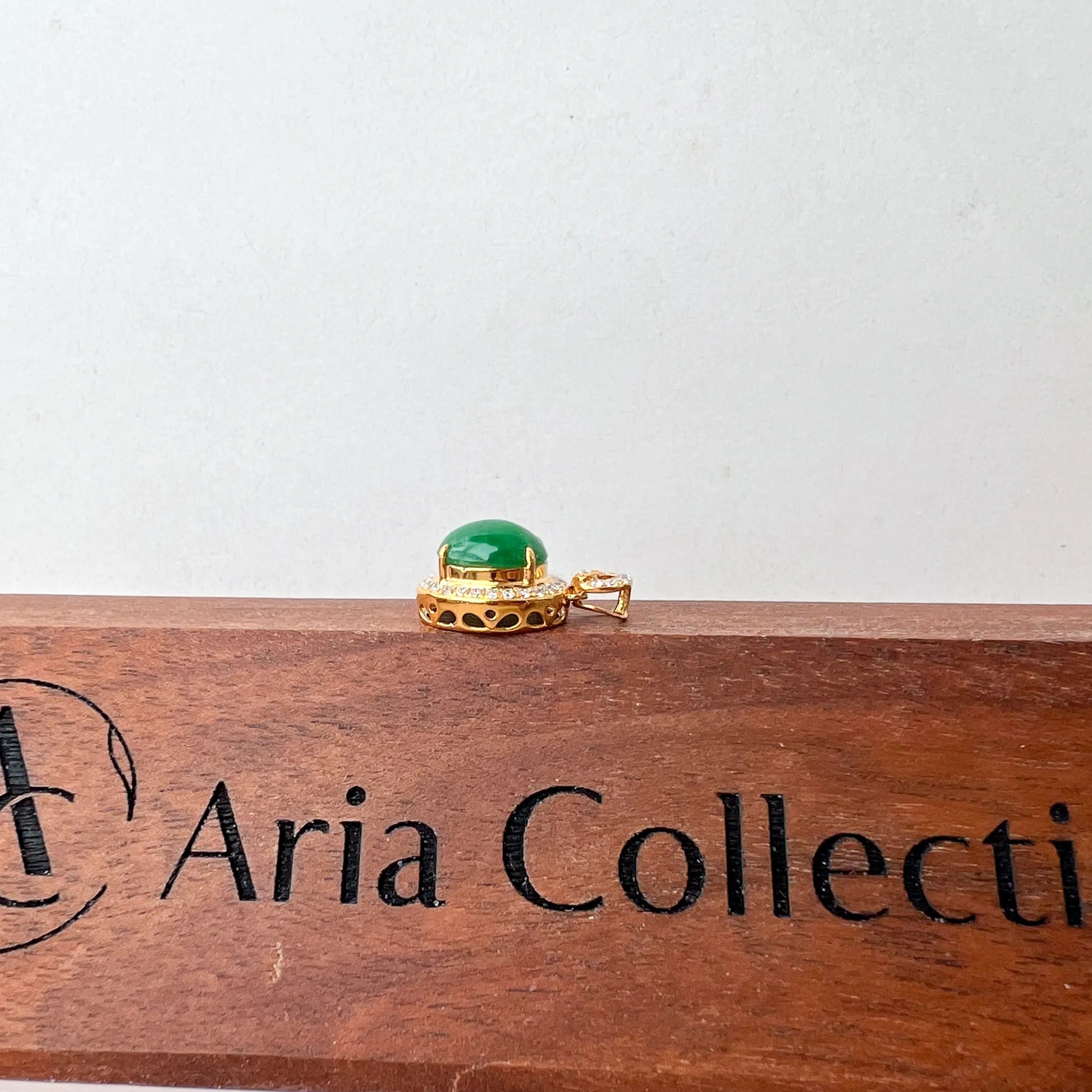 Side profile of gold pendant showing raised green cabochon and openwork gallery on wood