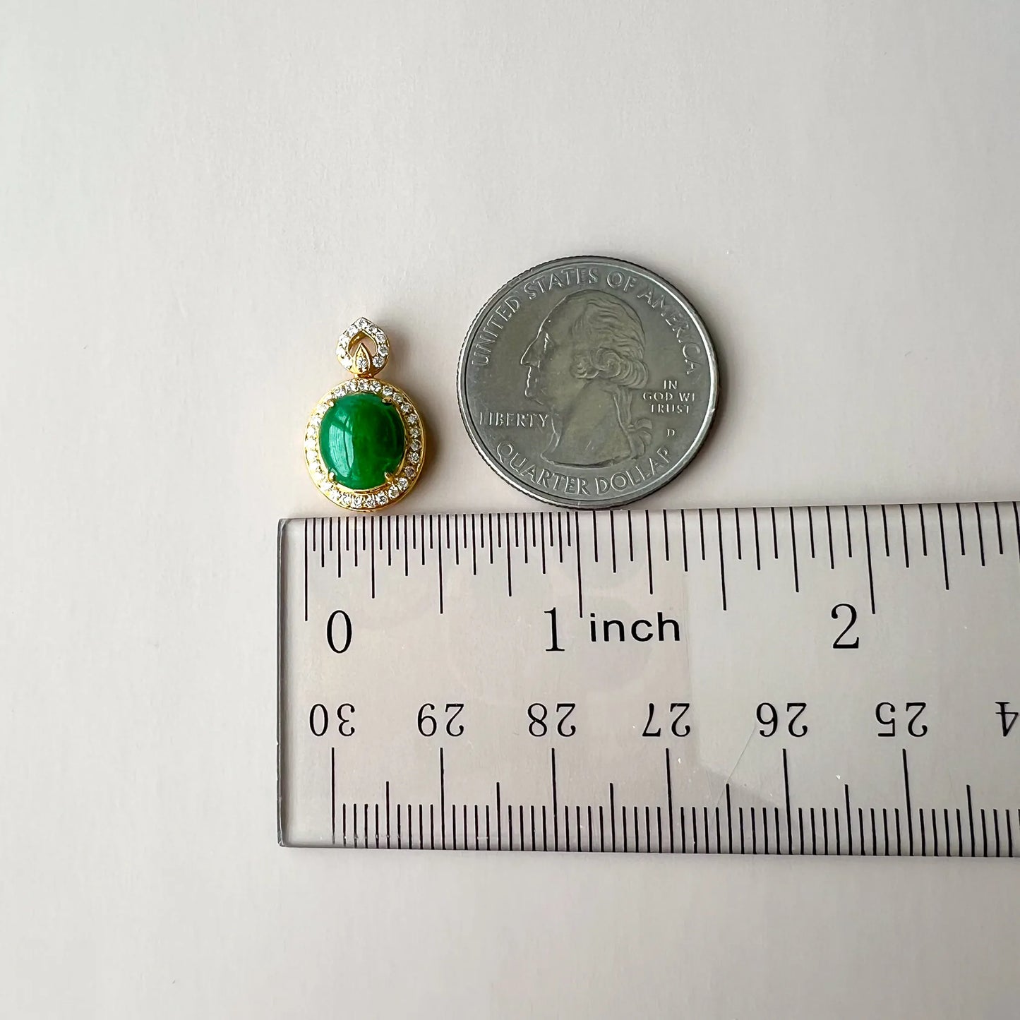 Pendant size reference beside ruler and quarter, small oval green gemstone in gold setting