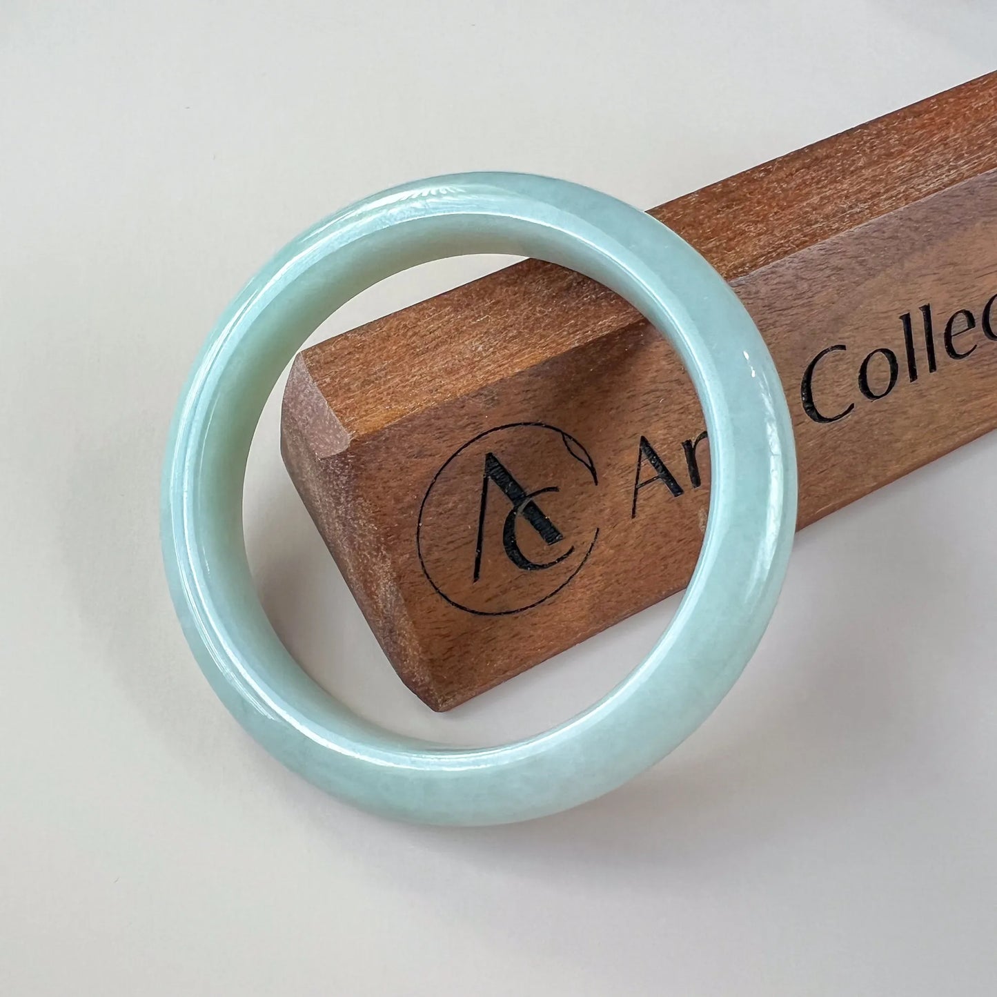 Glossy pale blue jade bangle displayed on a wooden stand, front view
