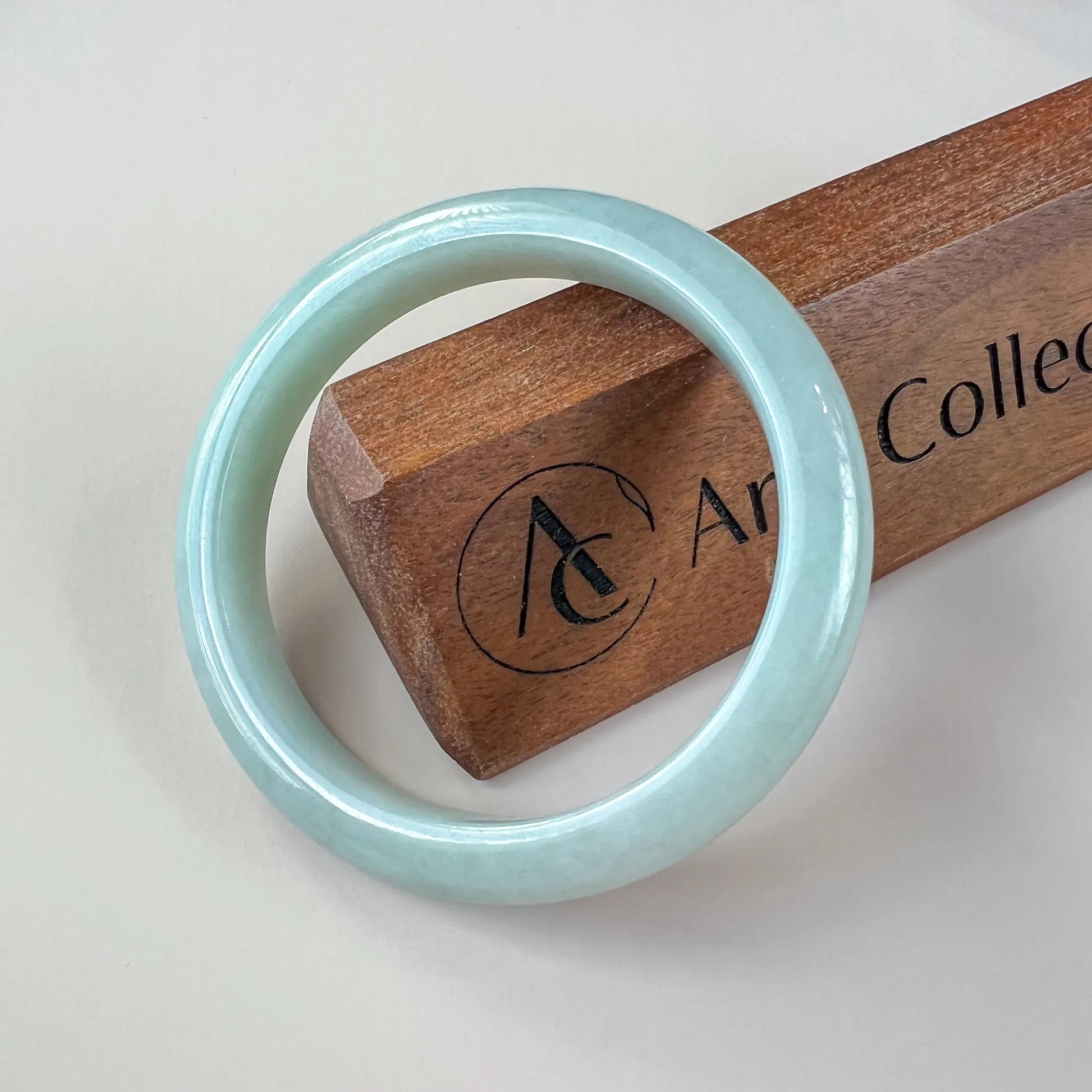 Glossy pale blue jade bangle displayed on a wooden stand, front view