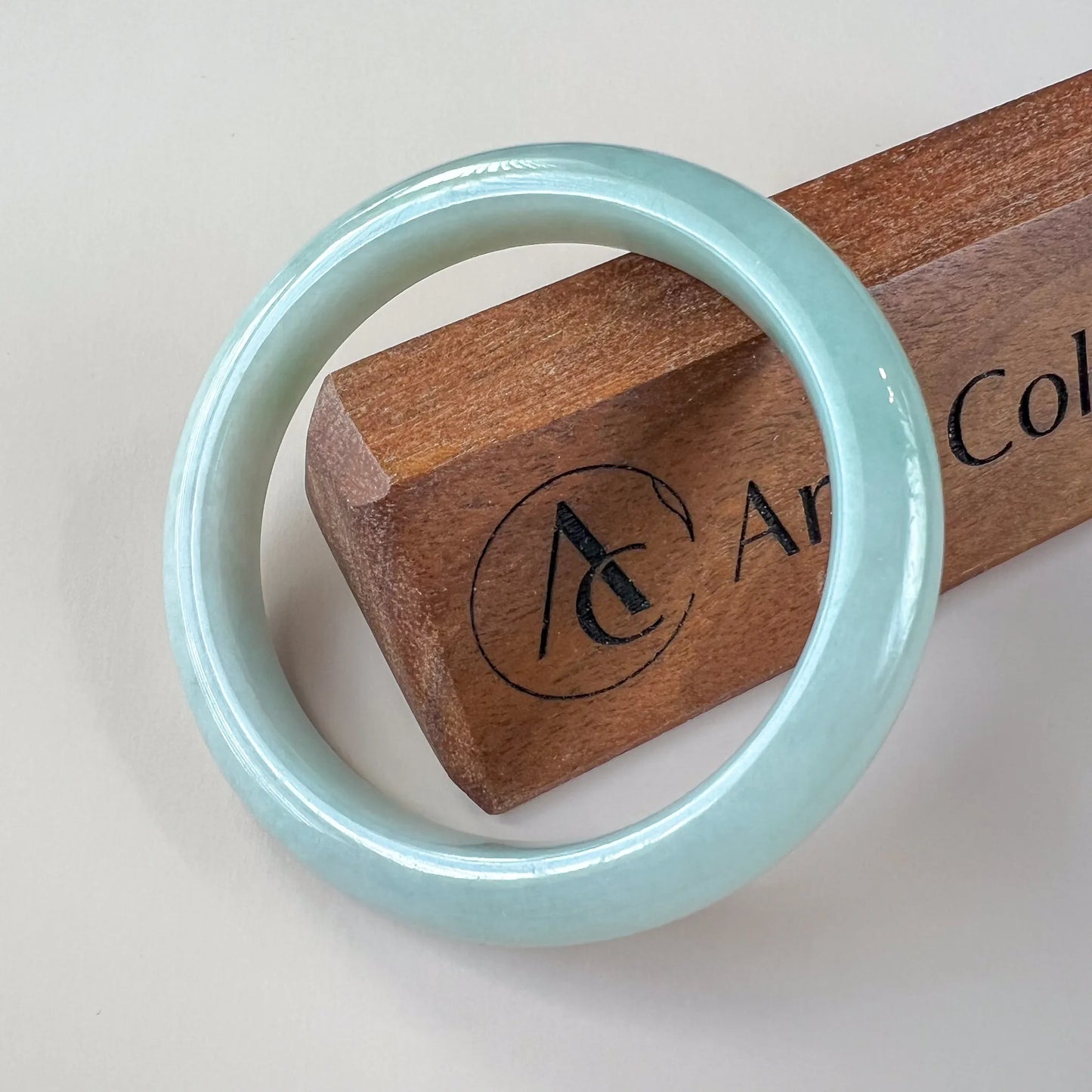 Smooth light blue jade bangle on a wooden display block, angled view