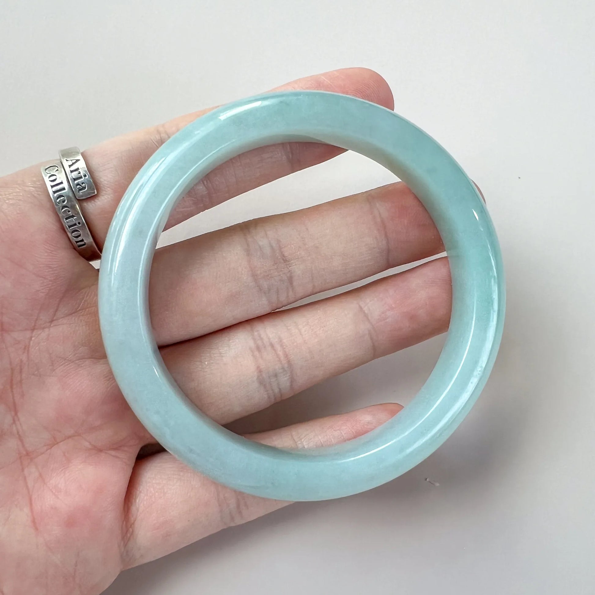 Round pale blue jade bangle shown on hand, polished finish