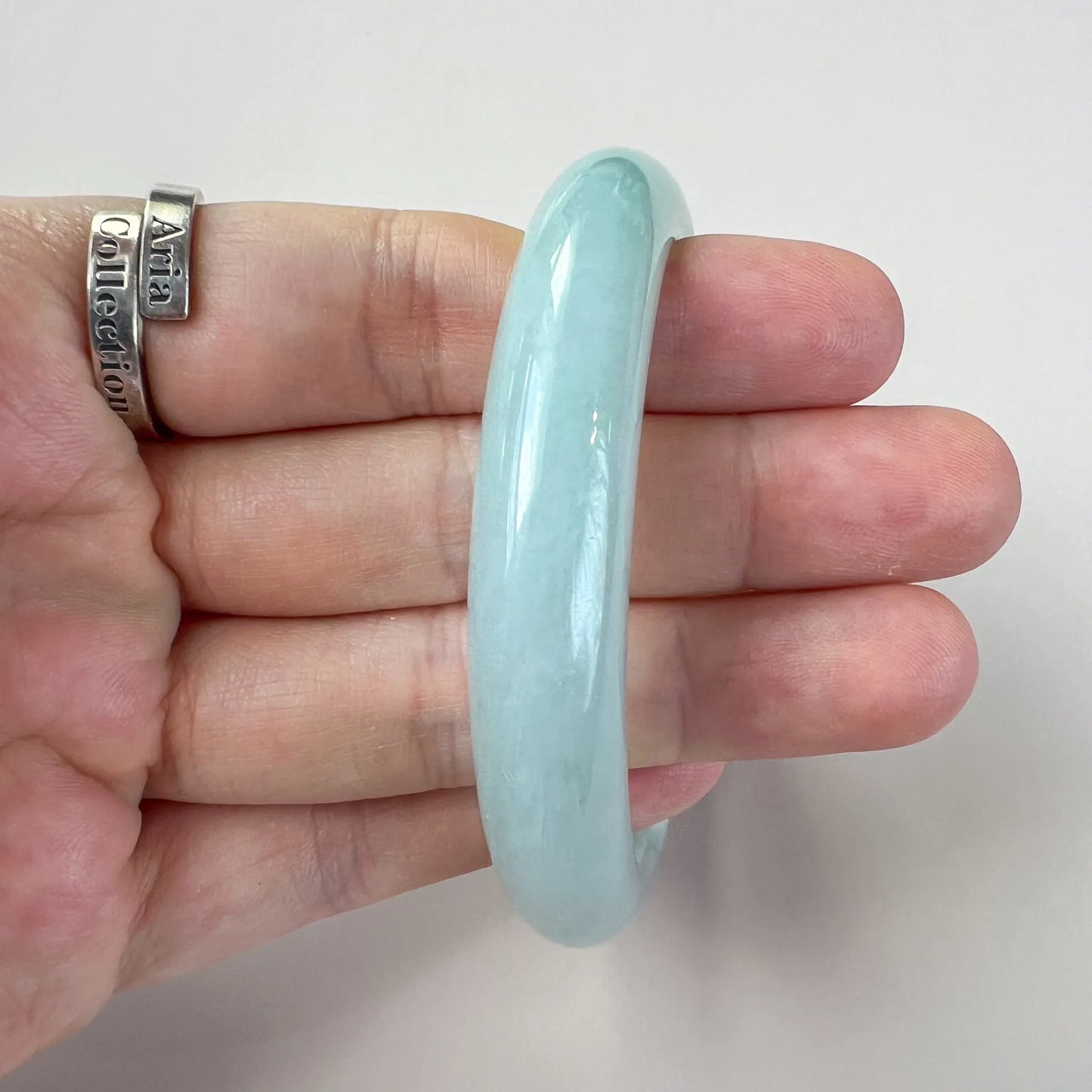 Side profile of glossy light blue jade bangle held against a hand