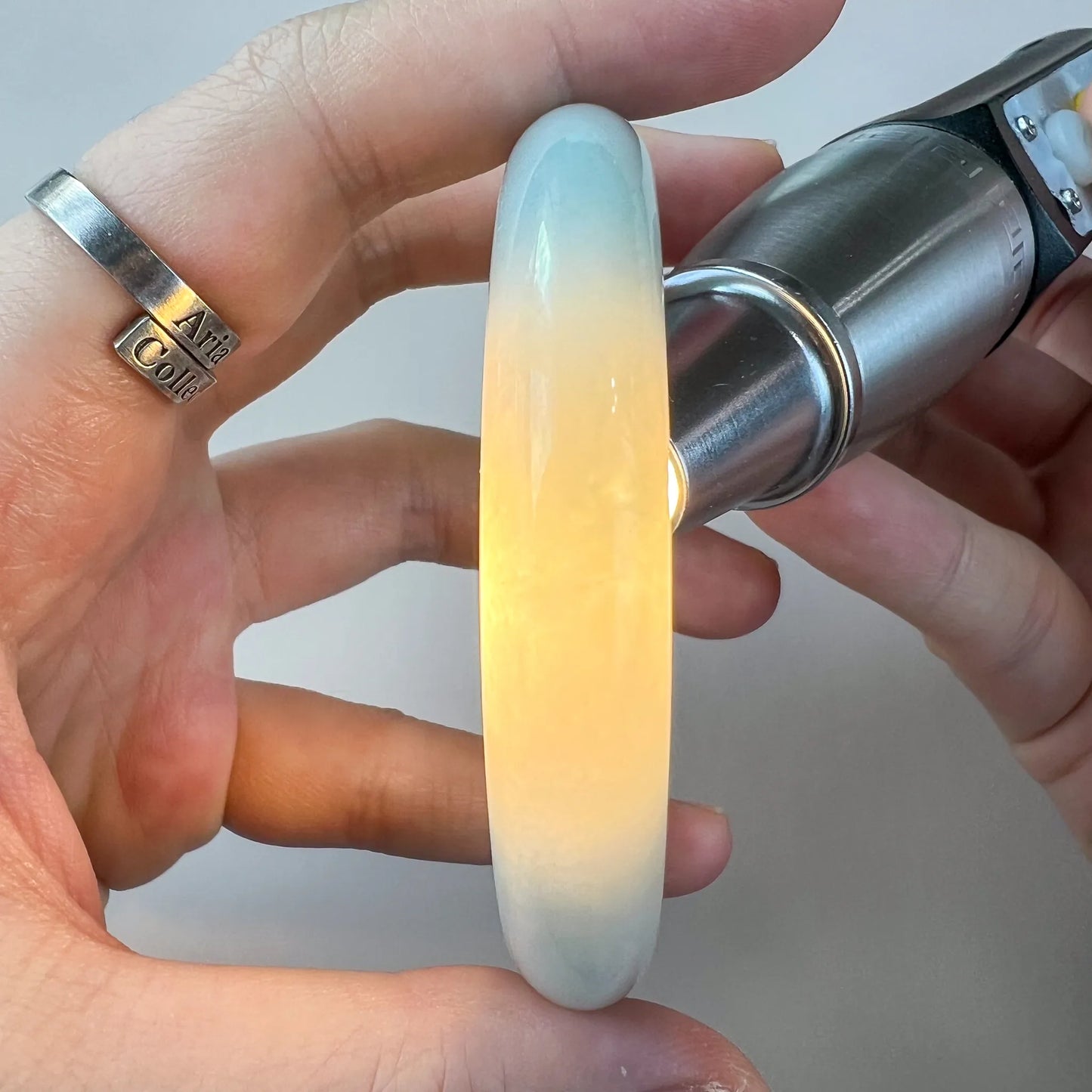 Backlit jade bangle with warm yellow center and pale blue edges, side view