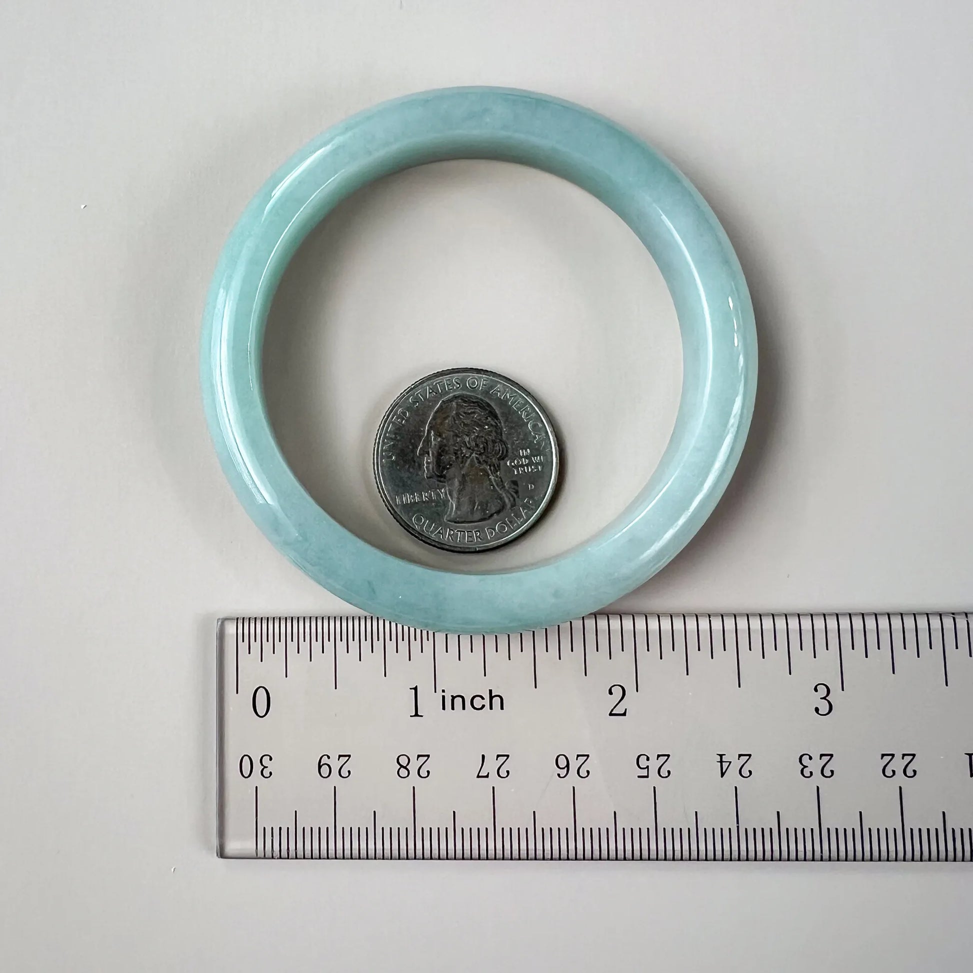 Light blue ring with a coin inside, next to a ruler for size reference on a white background