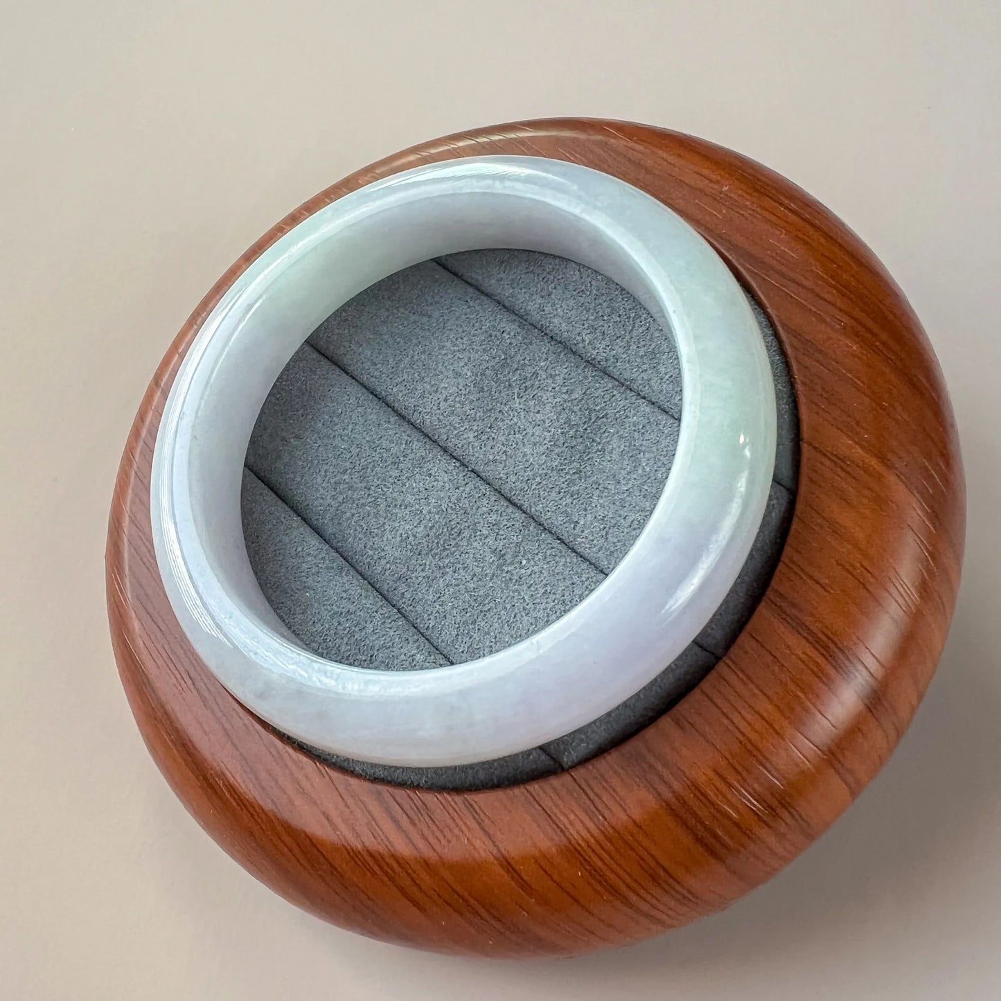 Angled view of pale blue jade bangle resting in a wooden jewelry stand, glossy finish