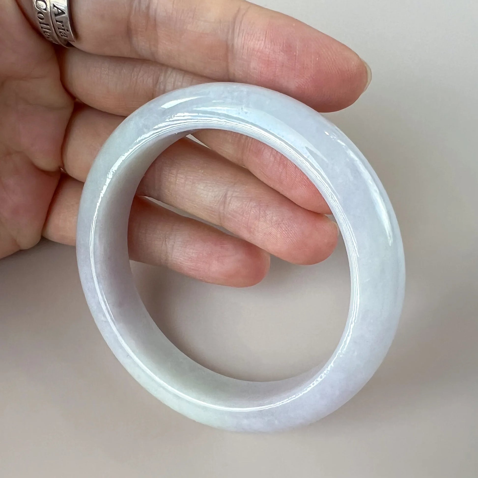 Handheld angled view of polished pale blue jade bangle showing smooth round form