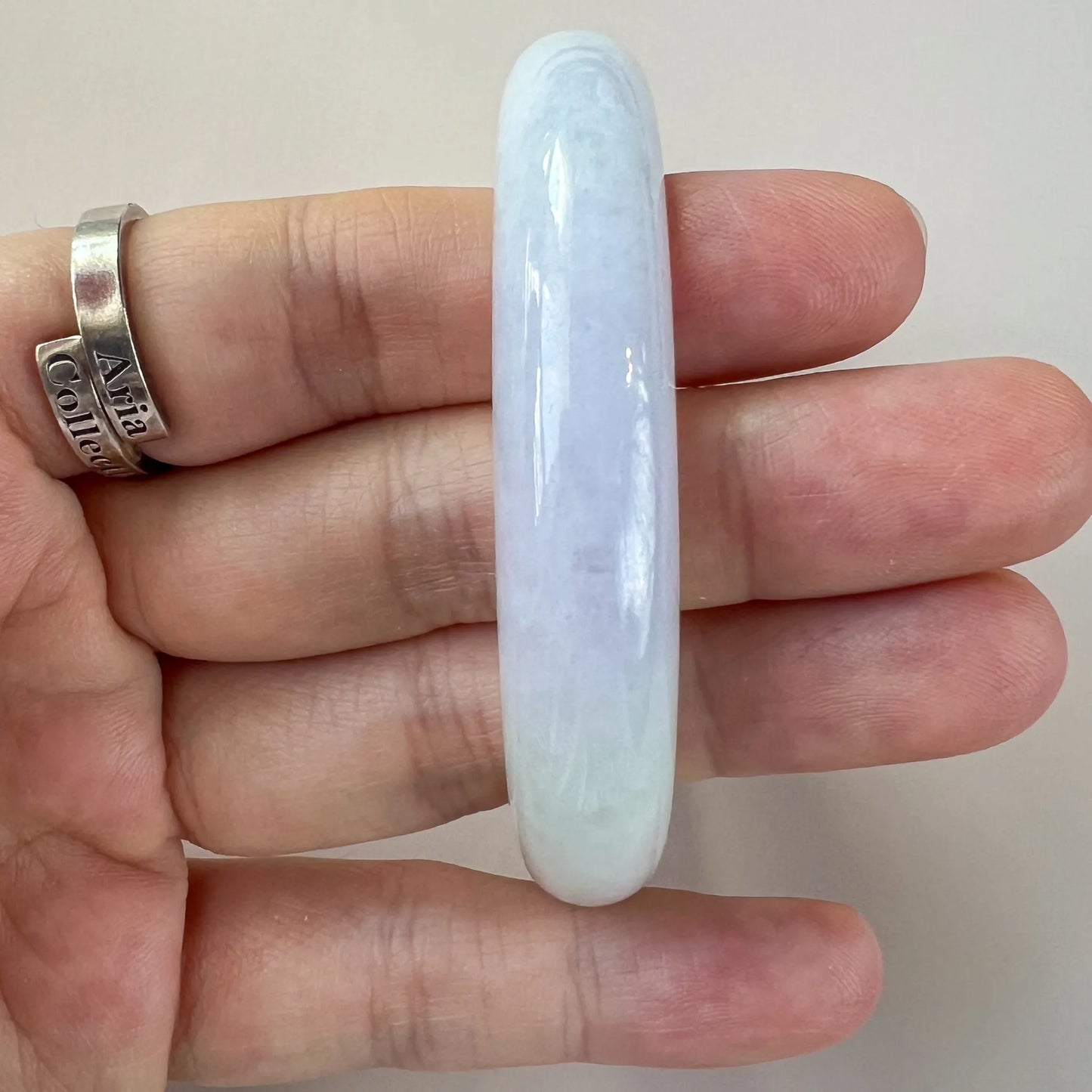 Side profile of slim pale blue jade bangle held in hand, glossy carved stone finish