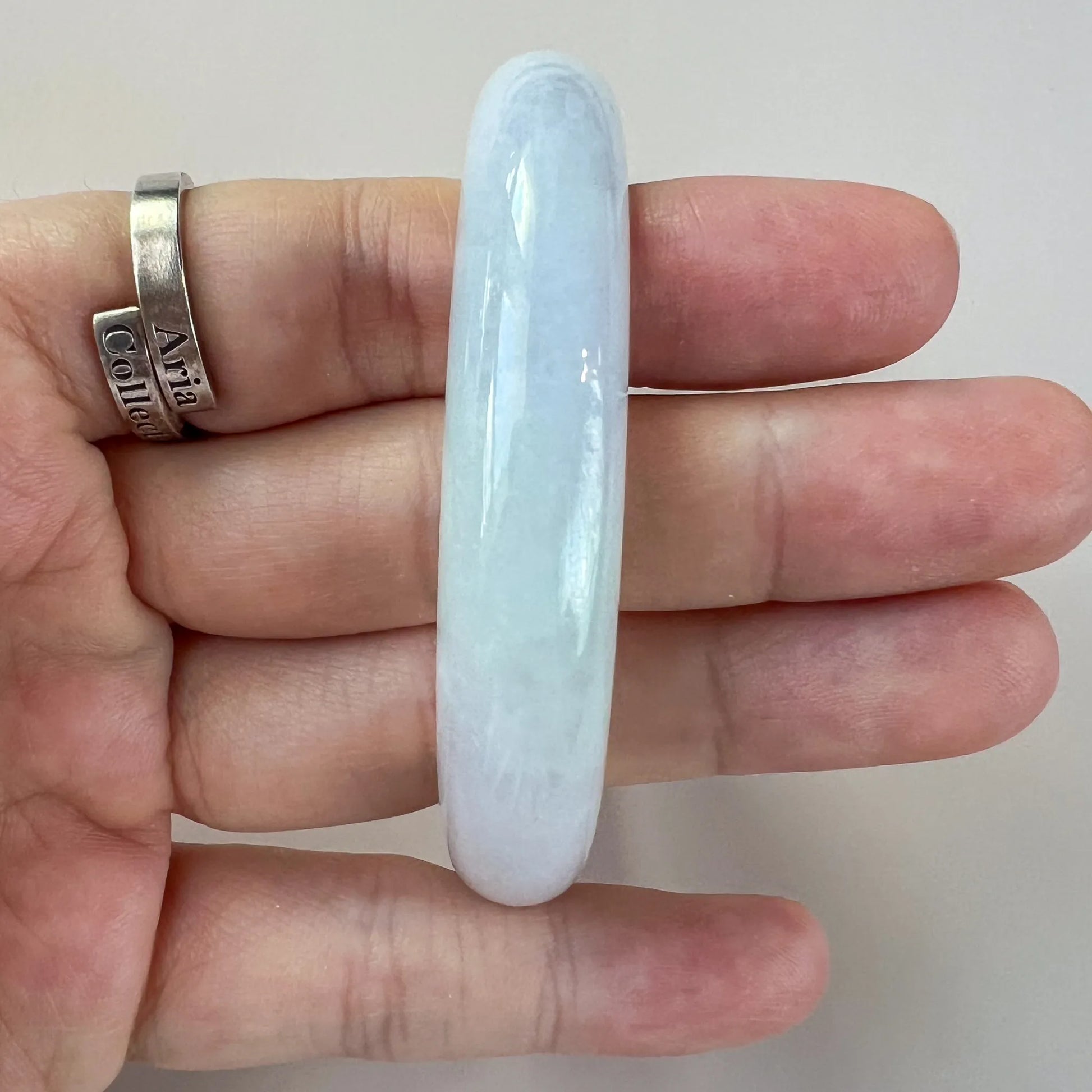 Vertical side view of pale blue jade bangle with polished smooth surface held in hand