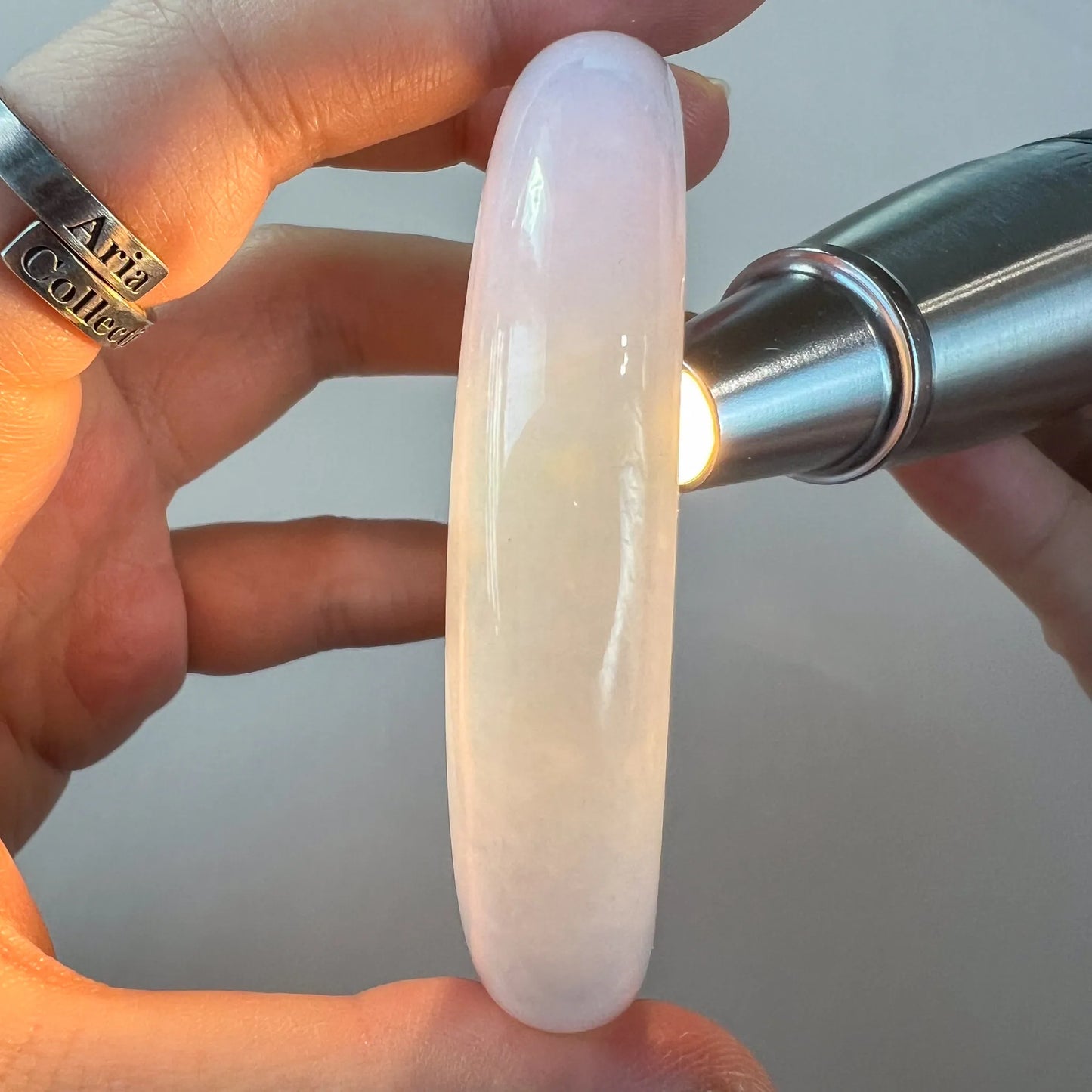 Translucent pale blue jade bangle held under flashlight to show stone color and clarity
