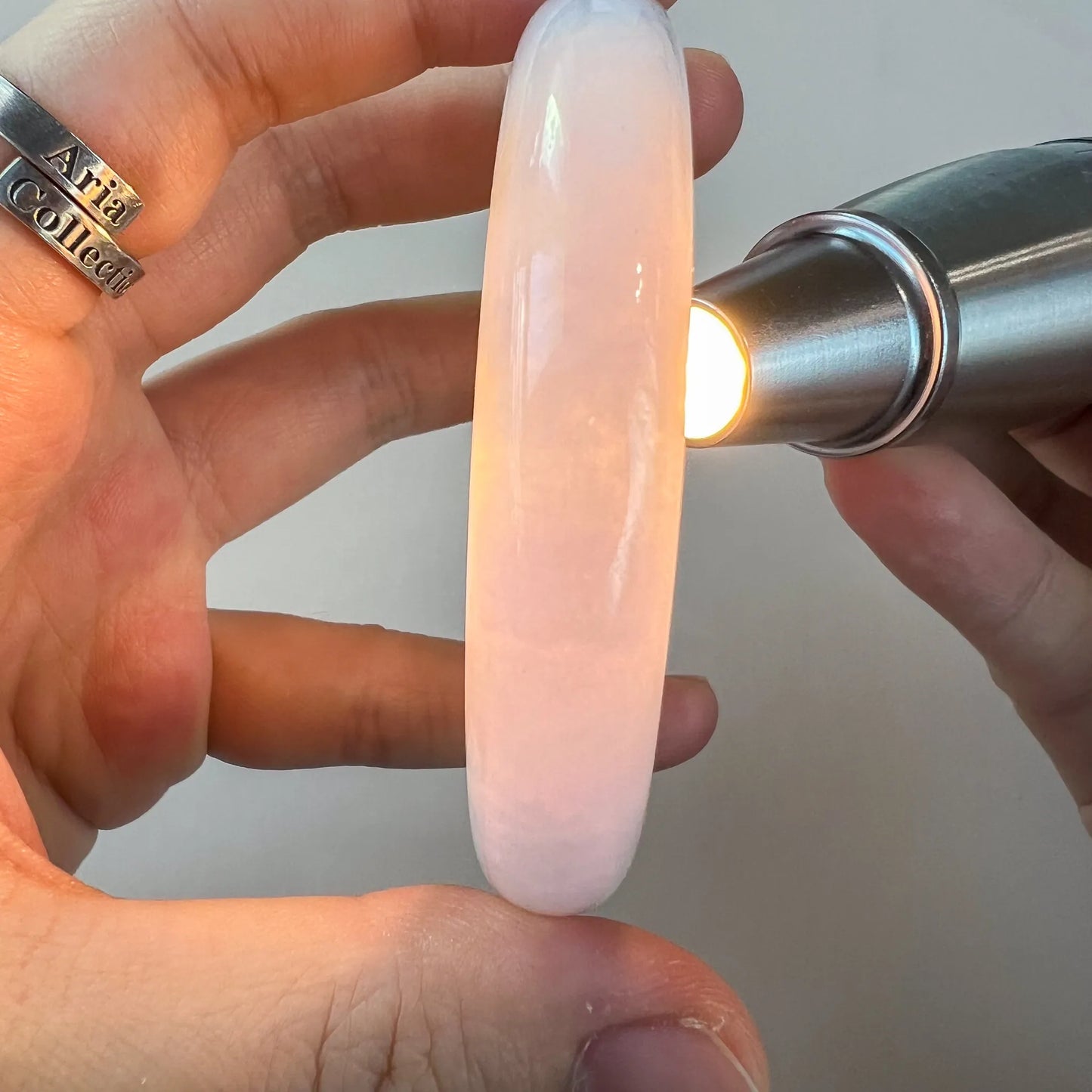 Translucent pink-toned jade bangle illuminated under flashlight, smooth polished finish