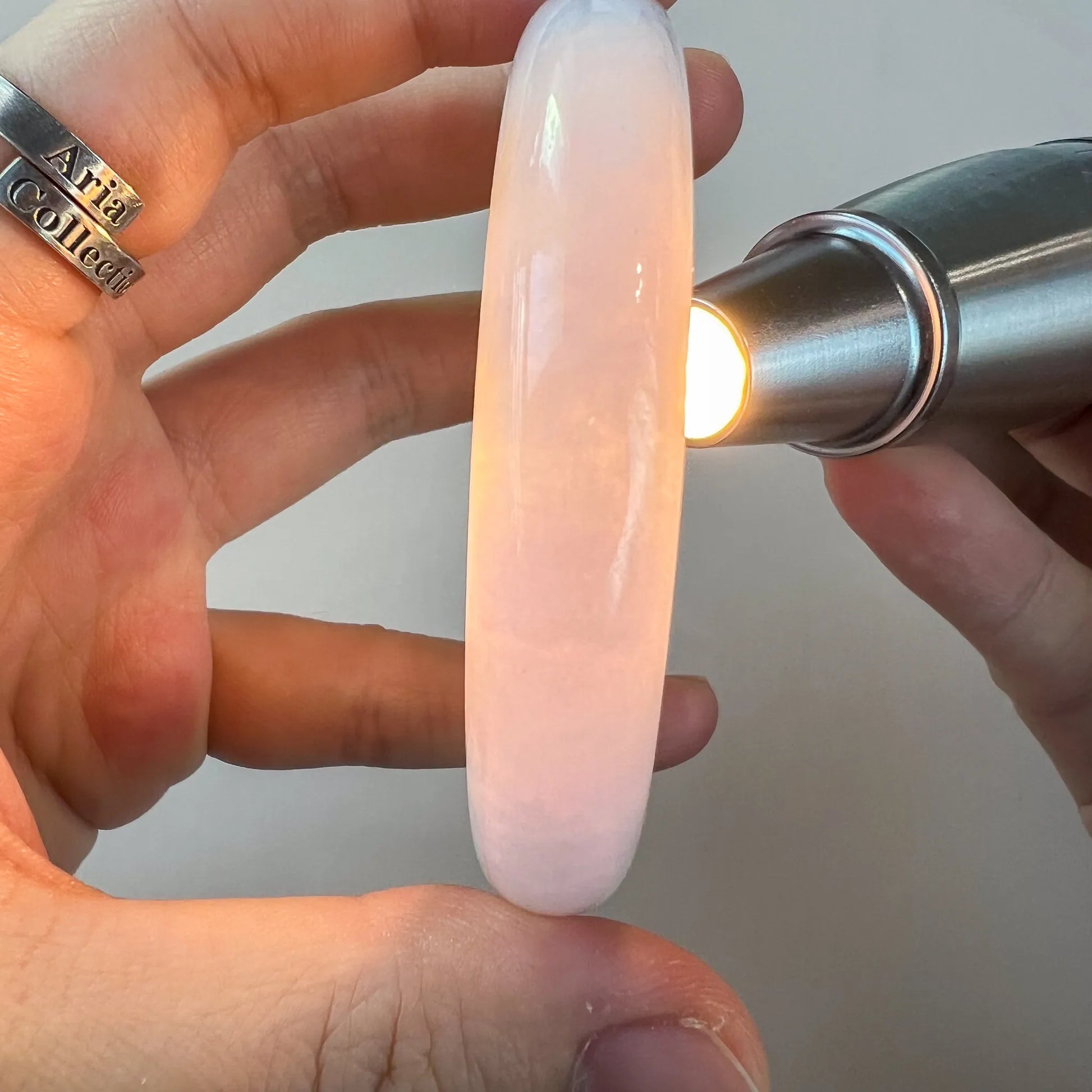 Translucent pink-toned jade bangle illuminated under flashlight, smooth polished finish