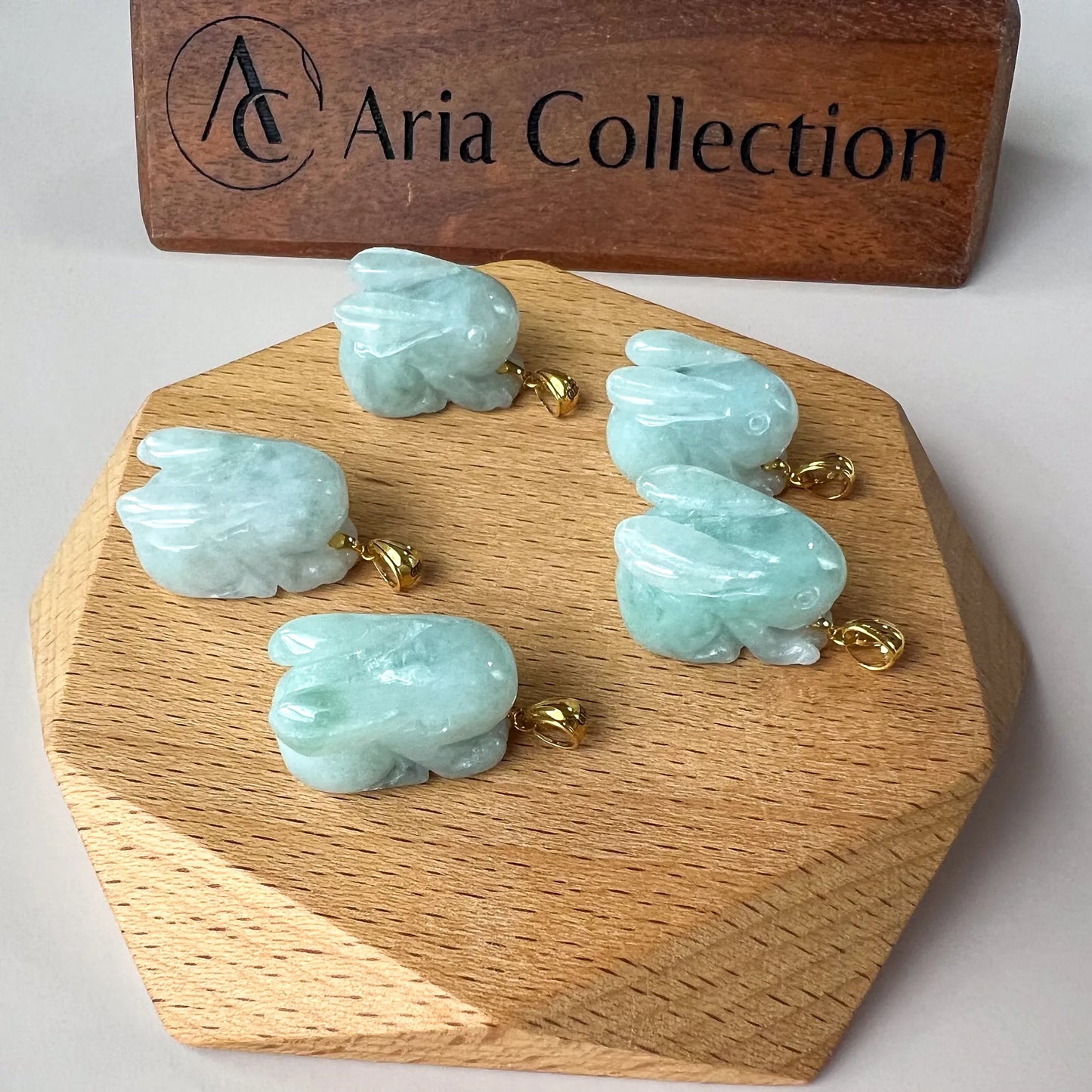 Top view of light blue jade rabbit pendant with polished gold bail on wood display