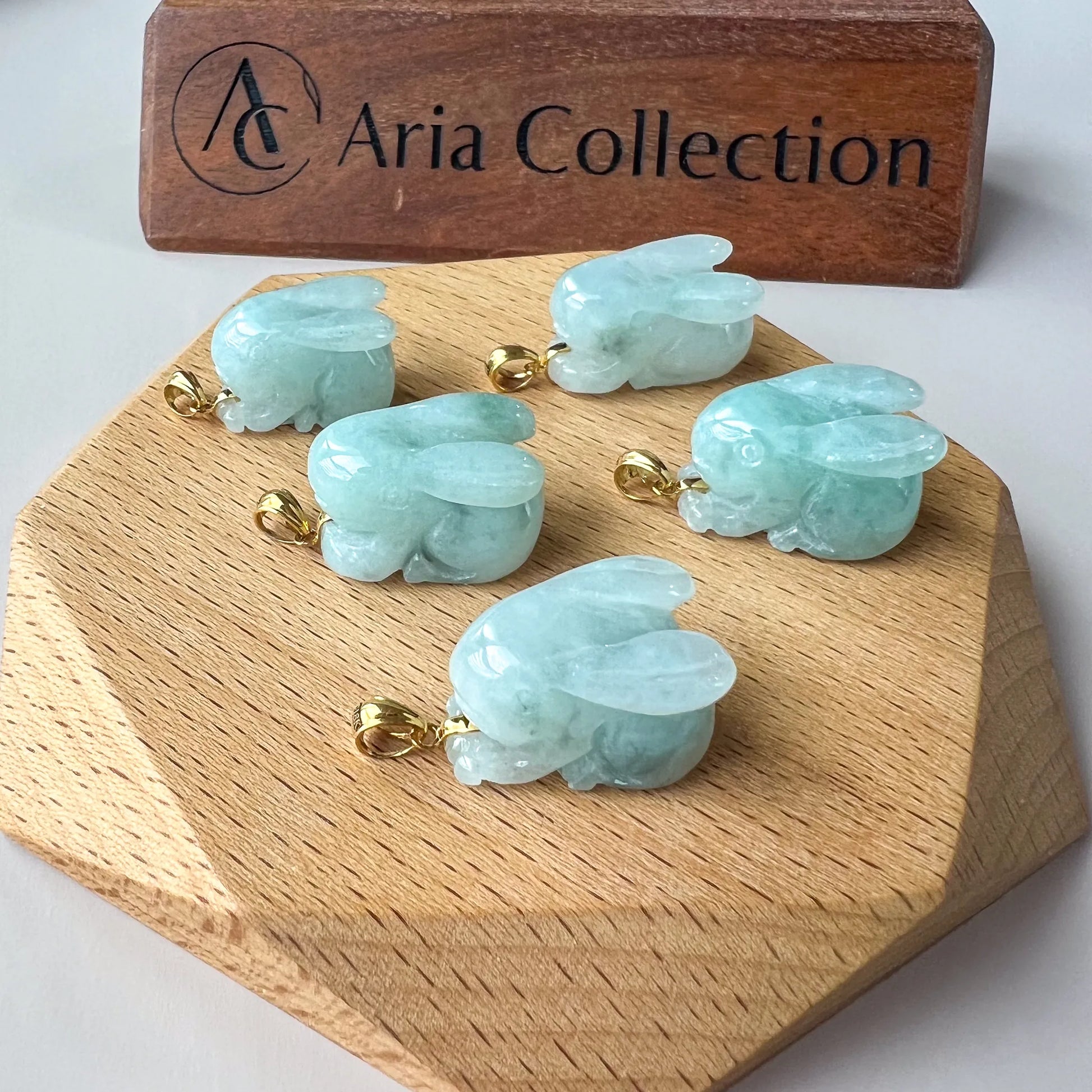 Cluster view of multiple polished jade rabbit pendants with gold bails on wooden stand