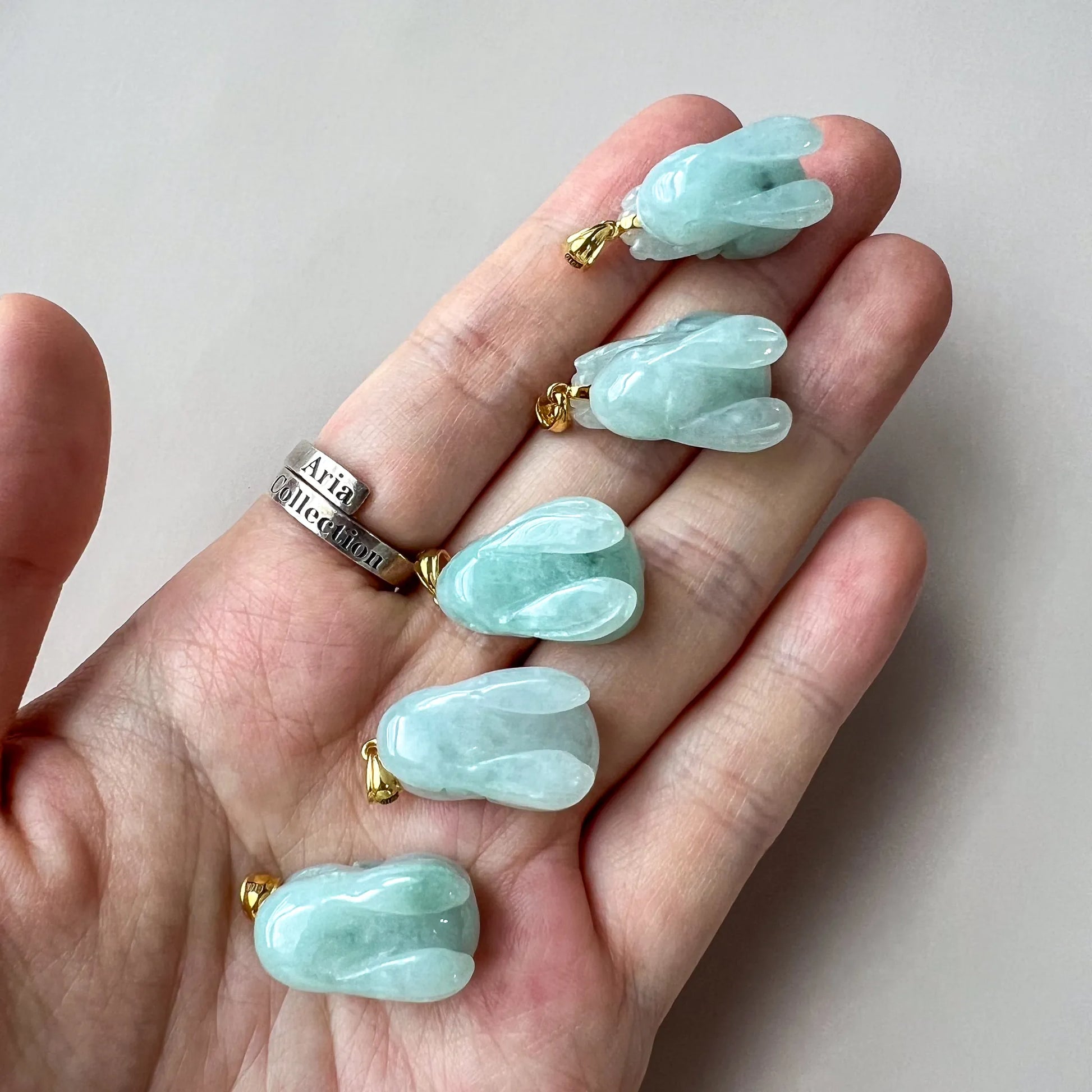 Hand scale view of glossy light blue jade rabbit pendants with gold bails