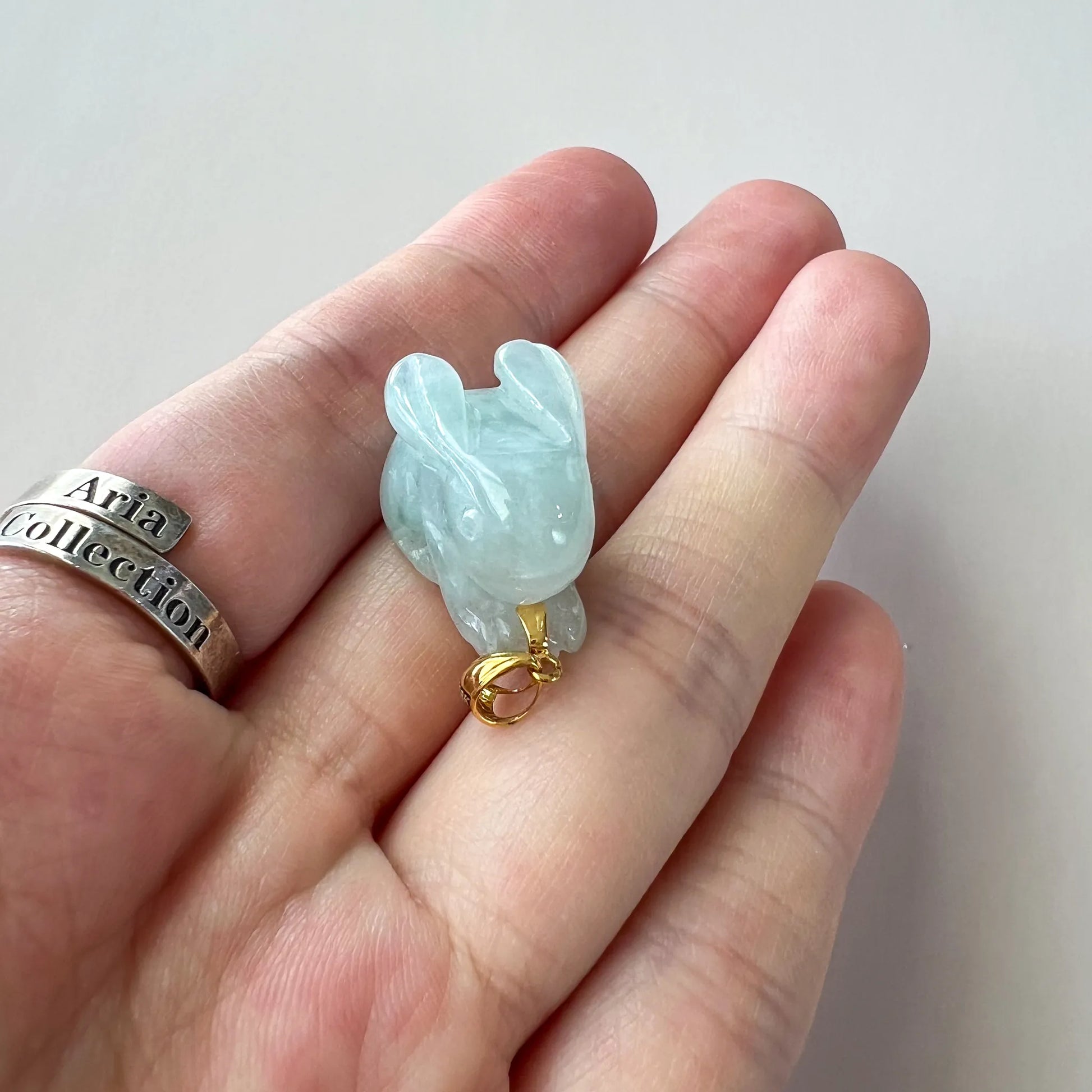Close-up of light green jadeite rabbit pendant, 3D carved polished stone with 18K gold bail held in hand