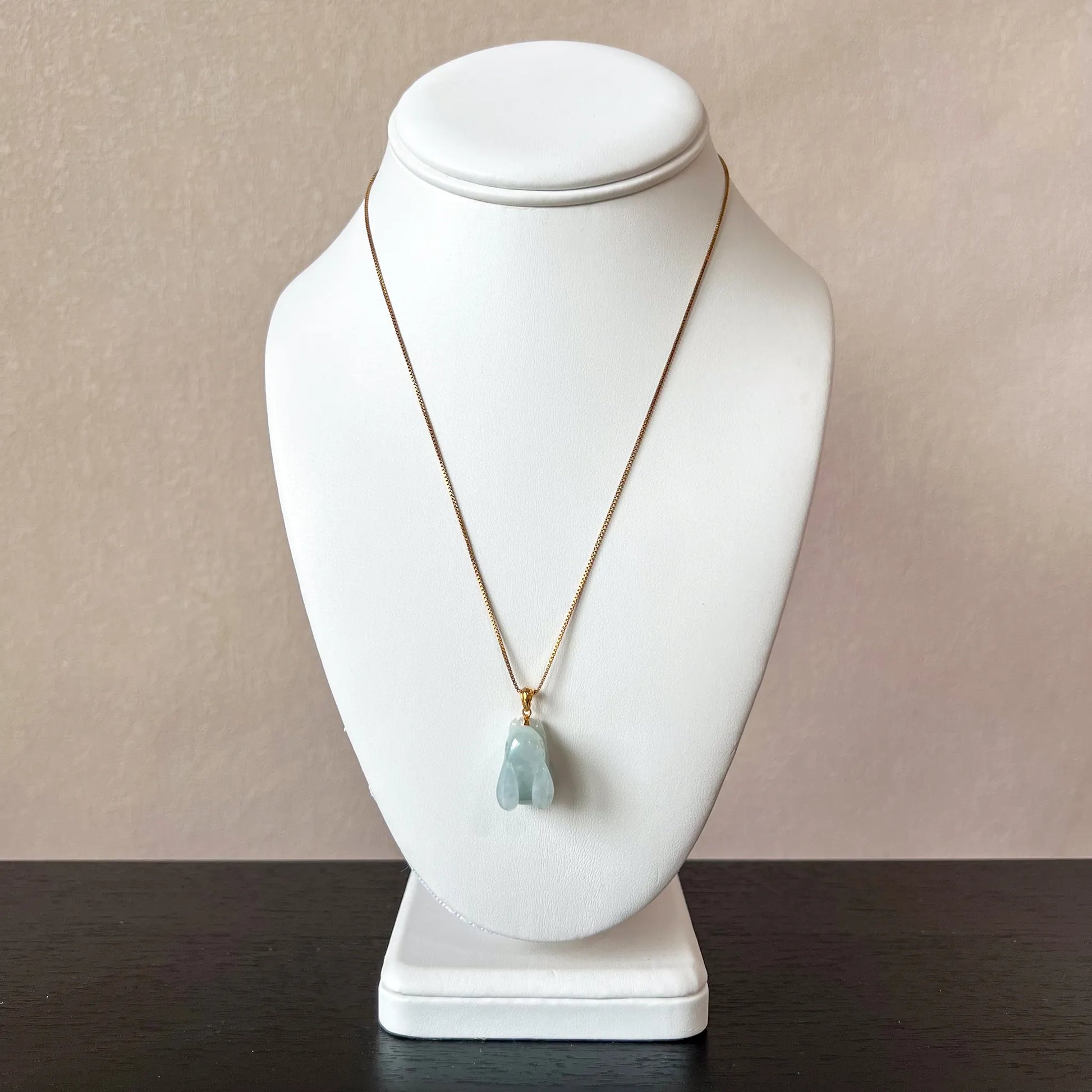 Light green 3D carved jadeite rabbit pendant with 18K gold bail on a fine gold chain, displayed on white bust