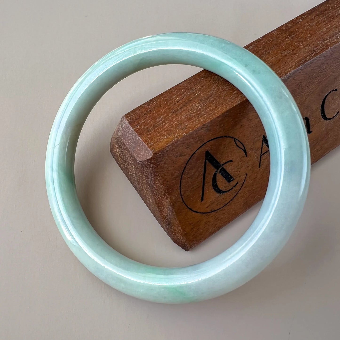 Glossy light jade bangle angled on a wooden display block, front view