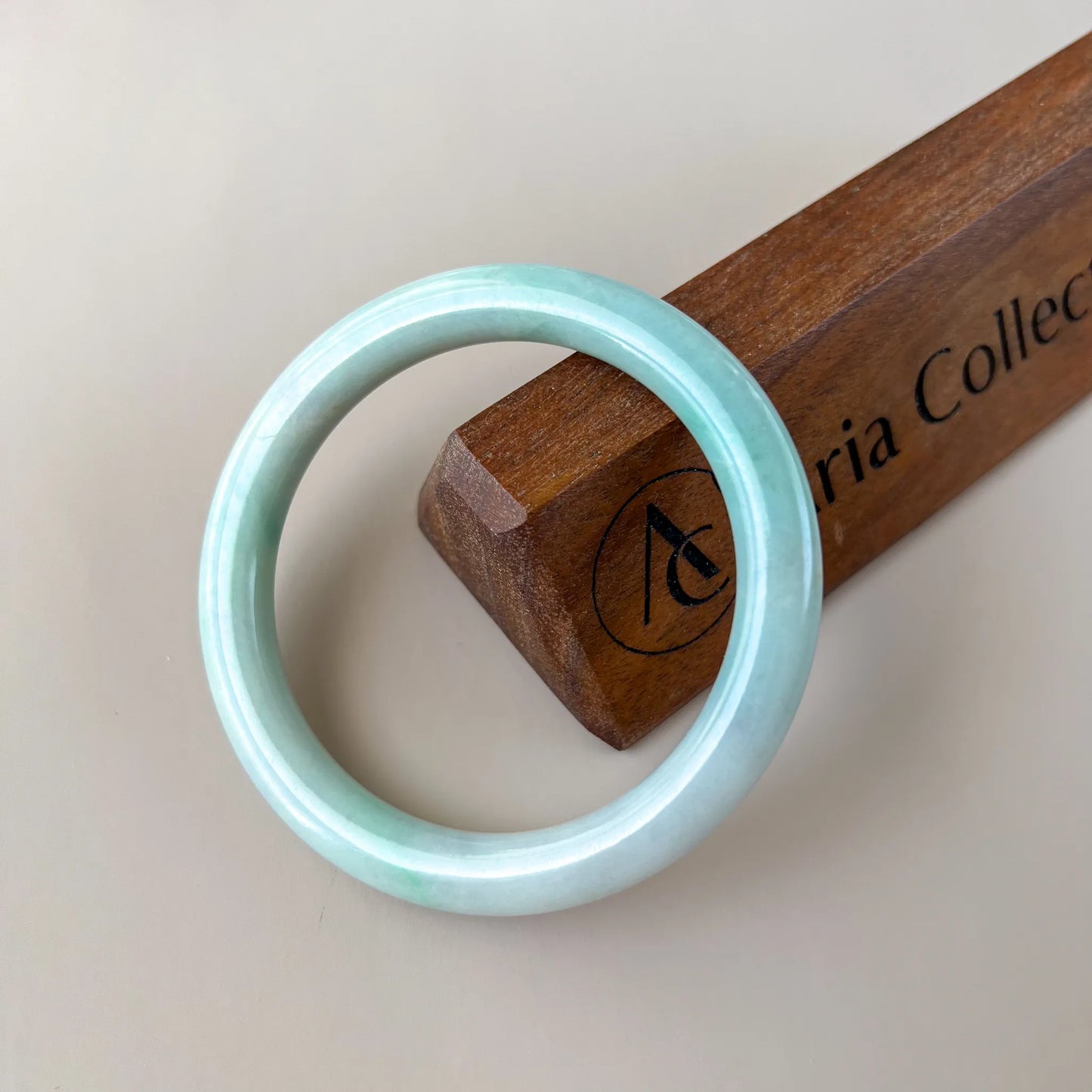 Polished pale green jade bangle leaning against a wooden display block, side angle