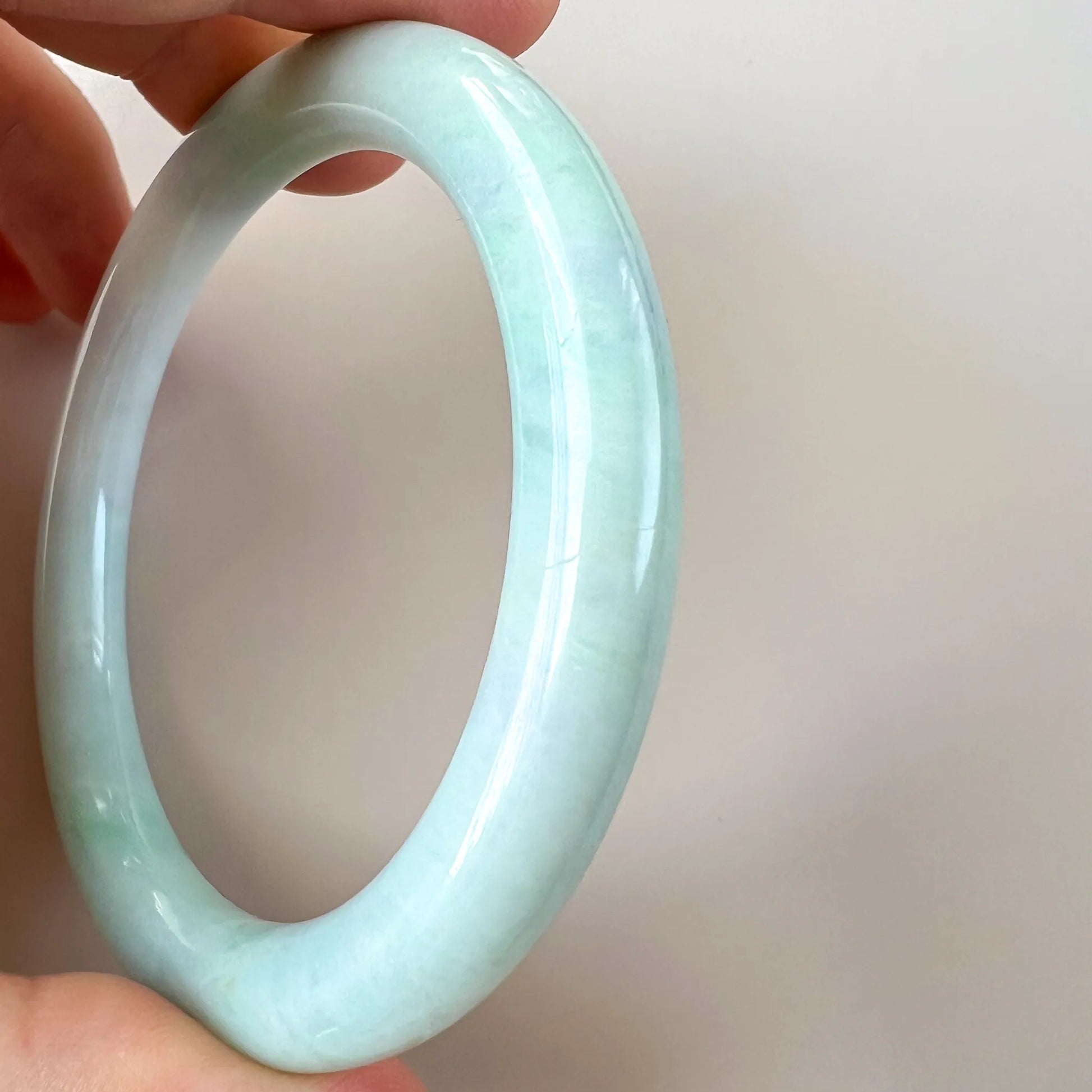 Handheld side view of polished pale green jade bangle with smooth finish