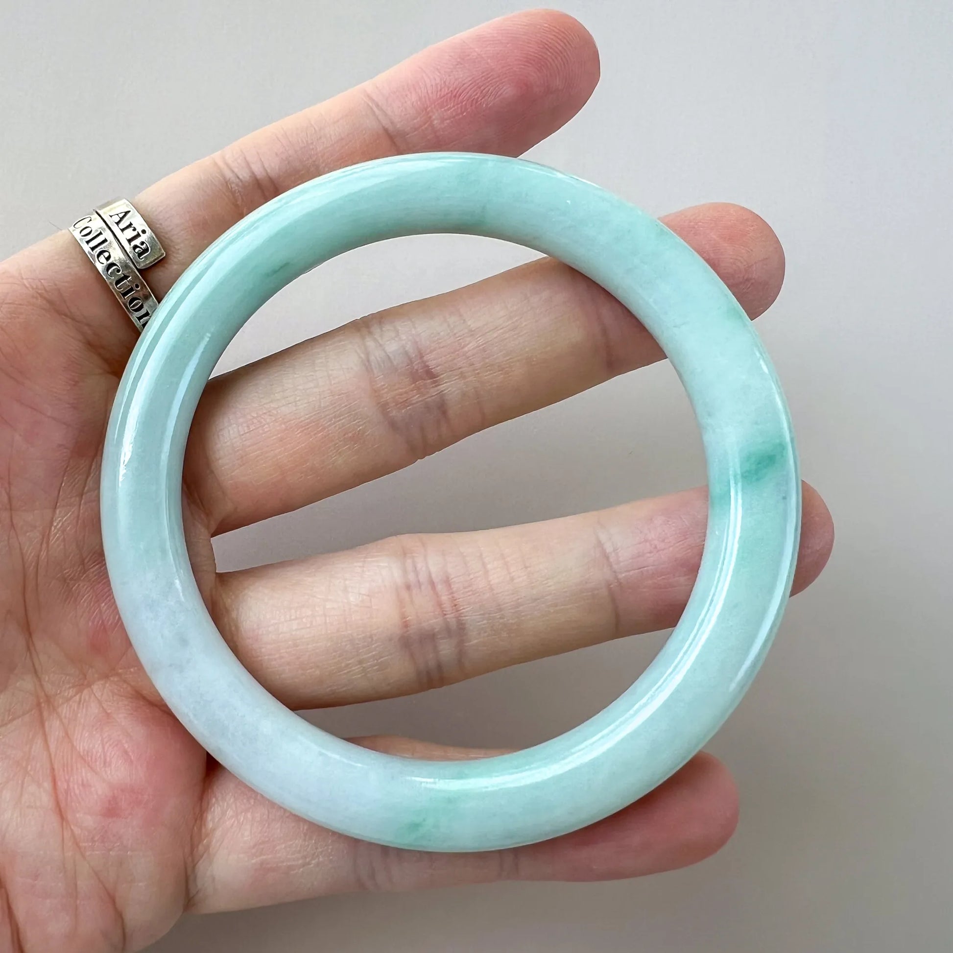 Handheld front view of glossy pale green jade bangle with translucent sheen