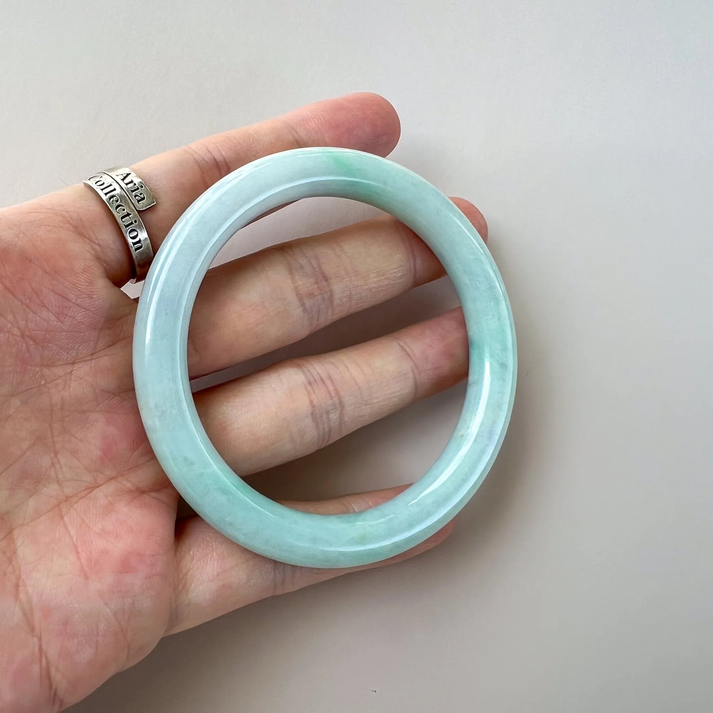 Handheld three-quarter view of smooth light green jade bangle