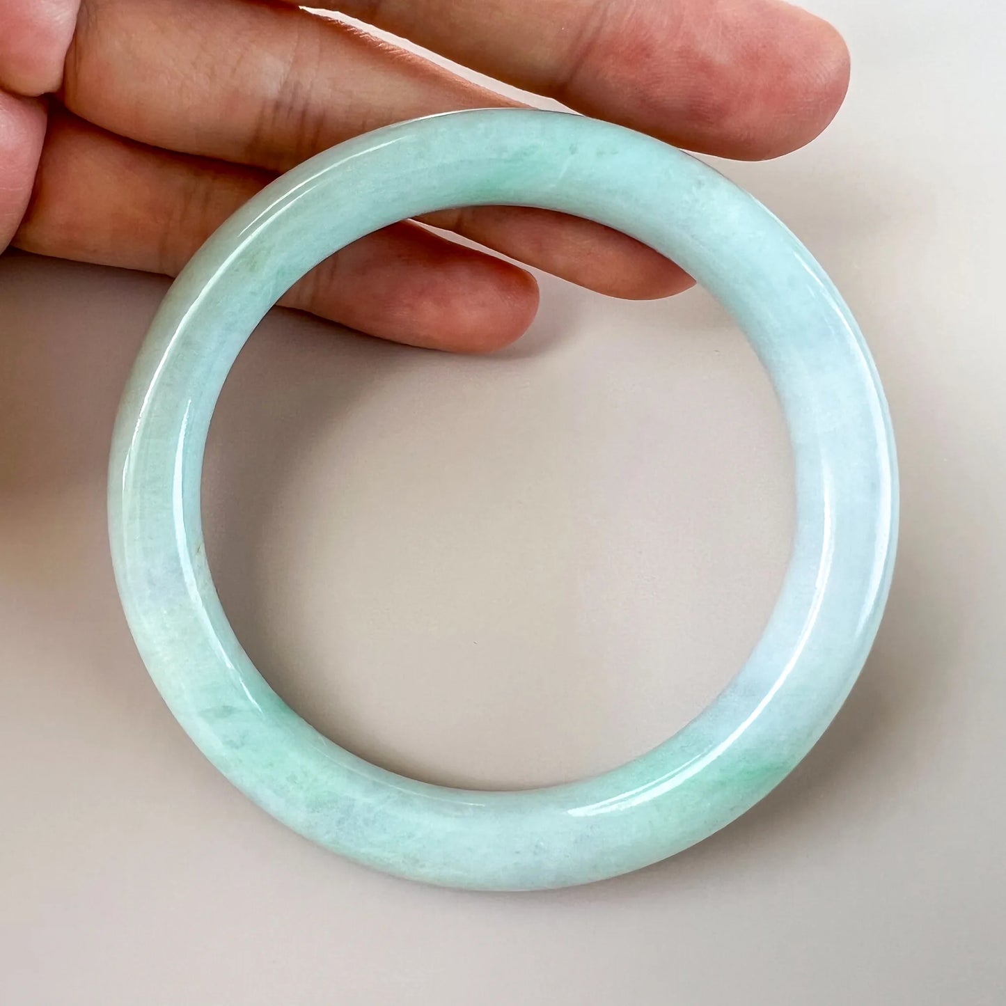 Handheld close view of polished pale jade bangle with even rounded edges