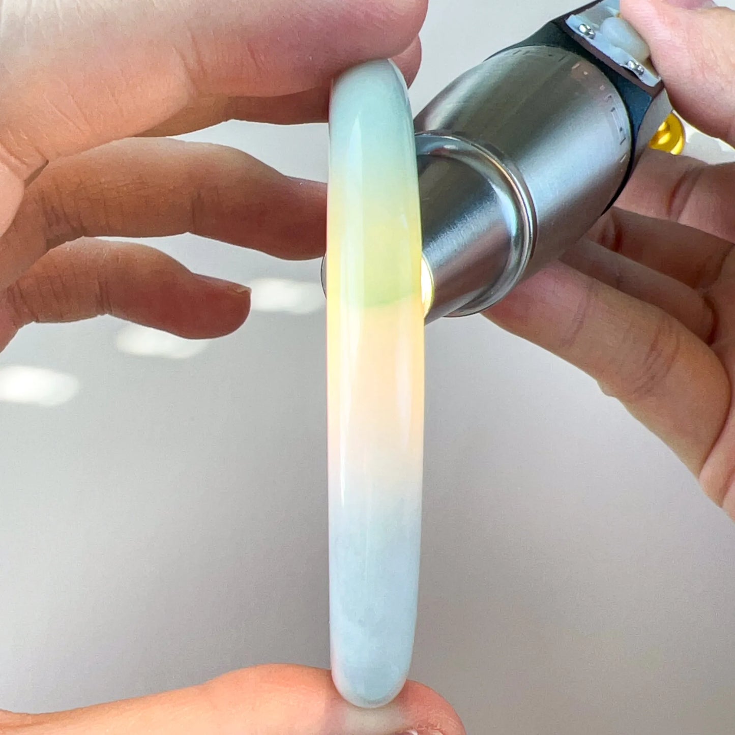 Side profile of translucent light green jade bangle held to light showing polished rounded edge