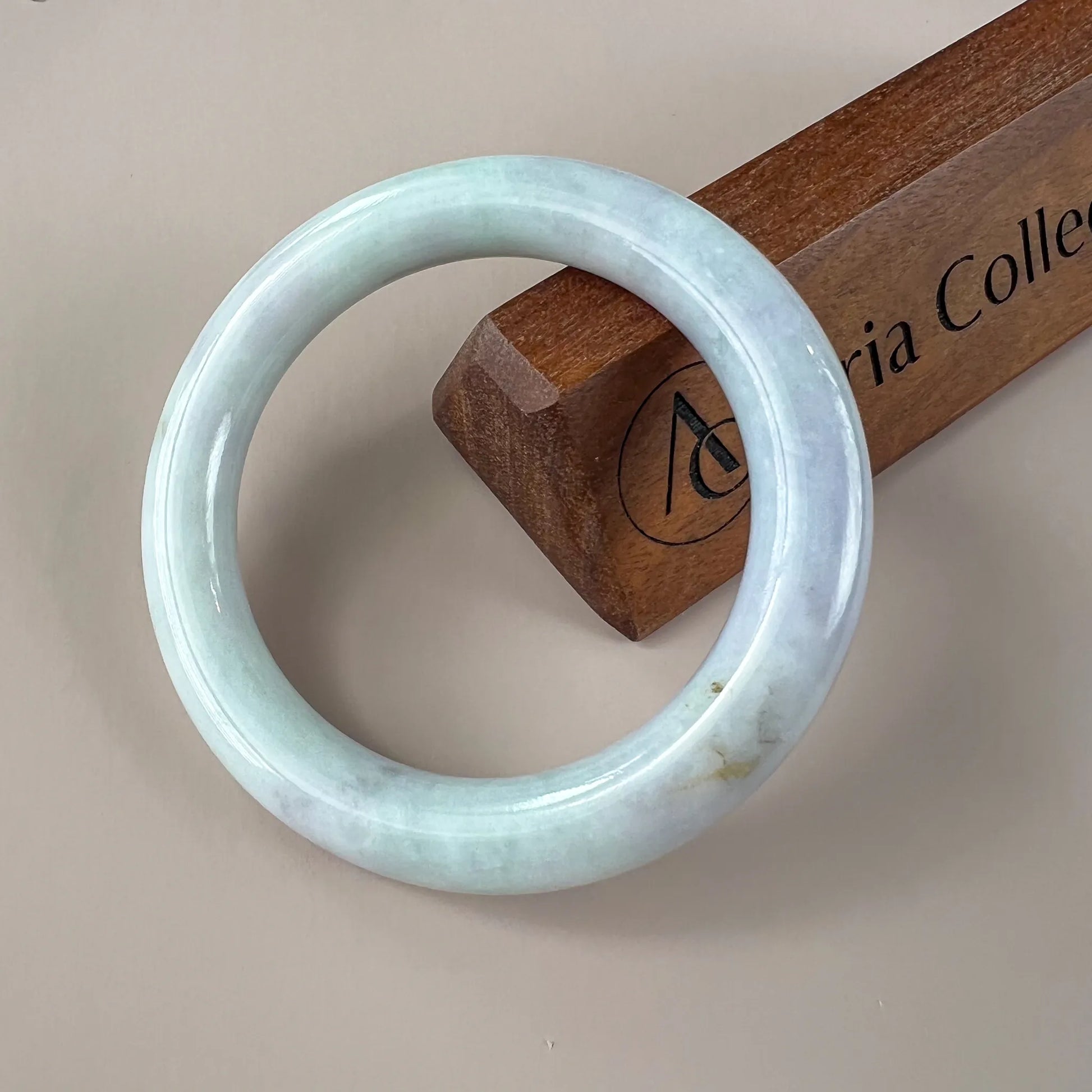Glossy pale blue jade bangle with smooth round profile on a wooden display block