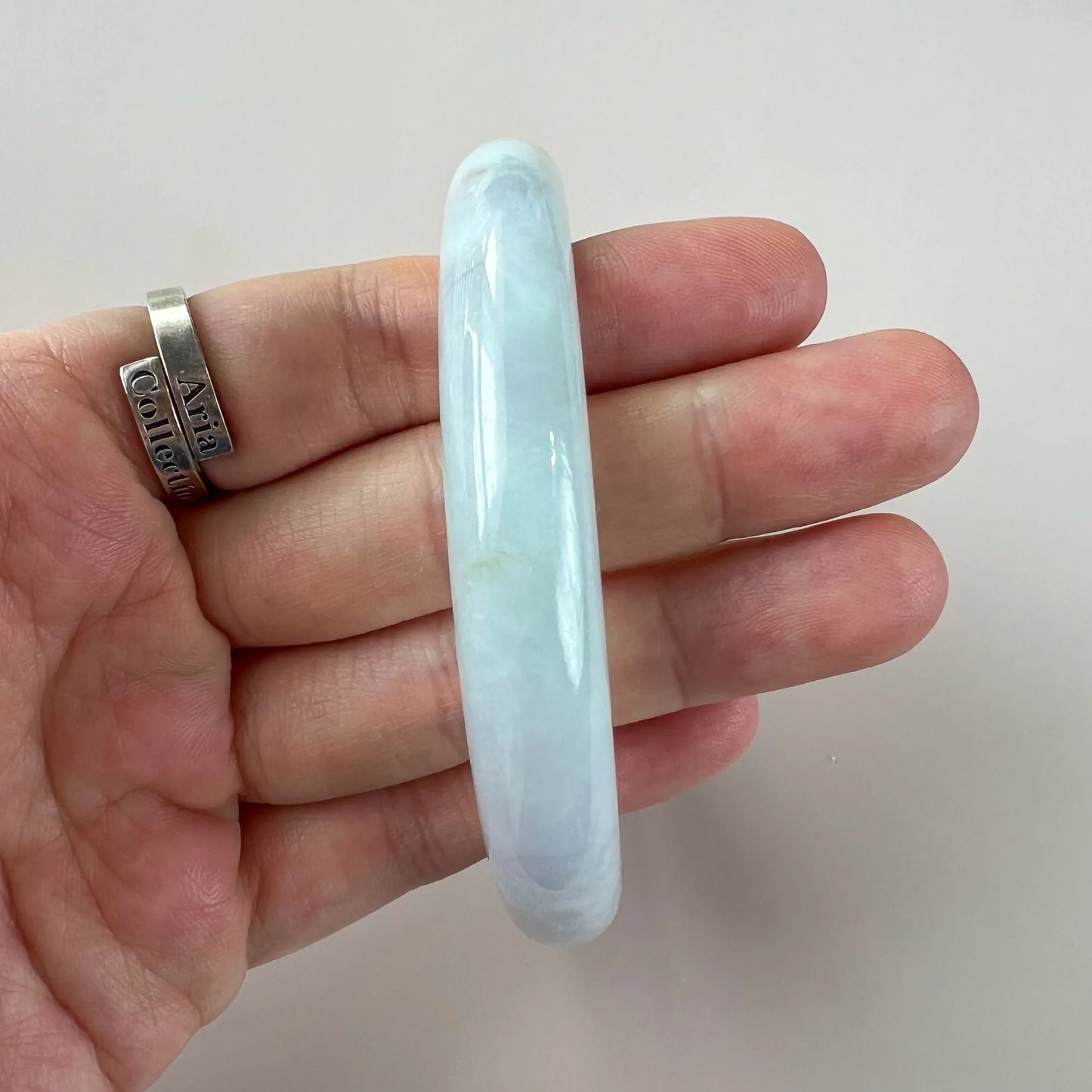 Side profile of smooth pale blue jade bangle shown in hand for scale