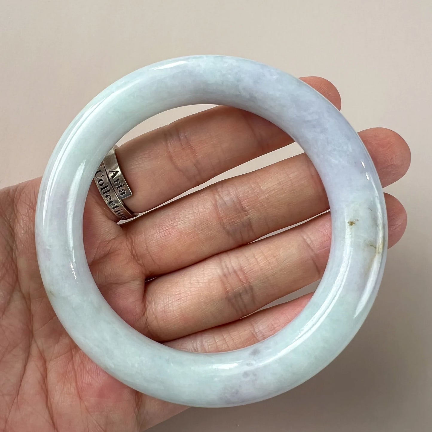Close hand view of polished pale blue jade bangle showing faint natural inclusions