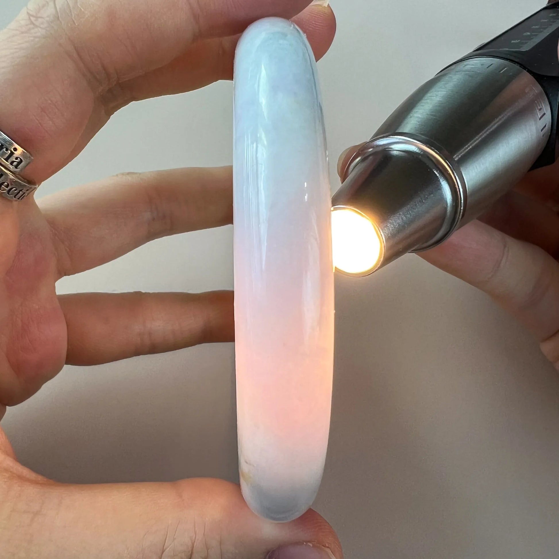 Side view of translucent pale blue jade bangle illuminated by flashlight