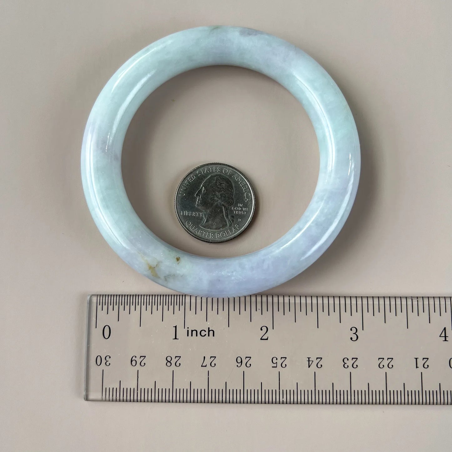 Pale green natural jade bangle shown with ruler and quarter for scale, polished rounded profile