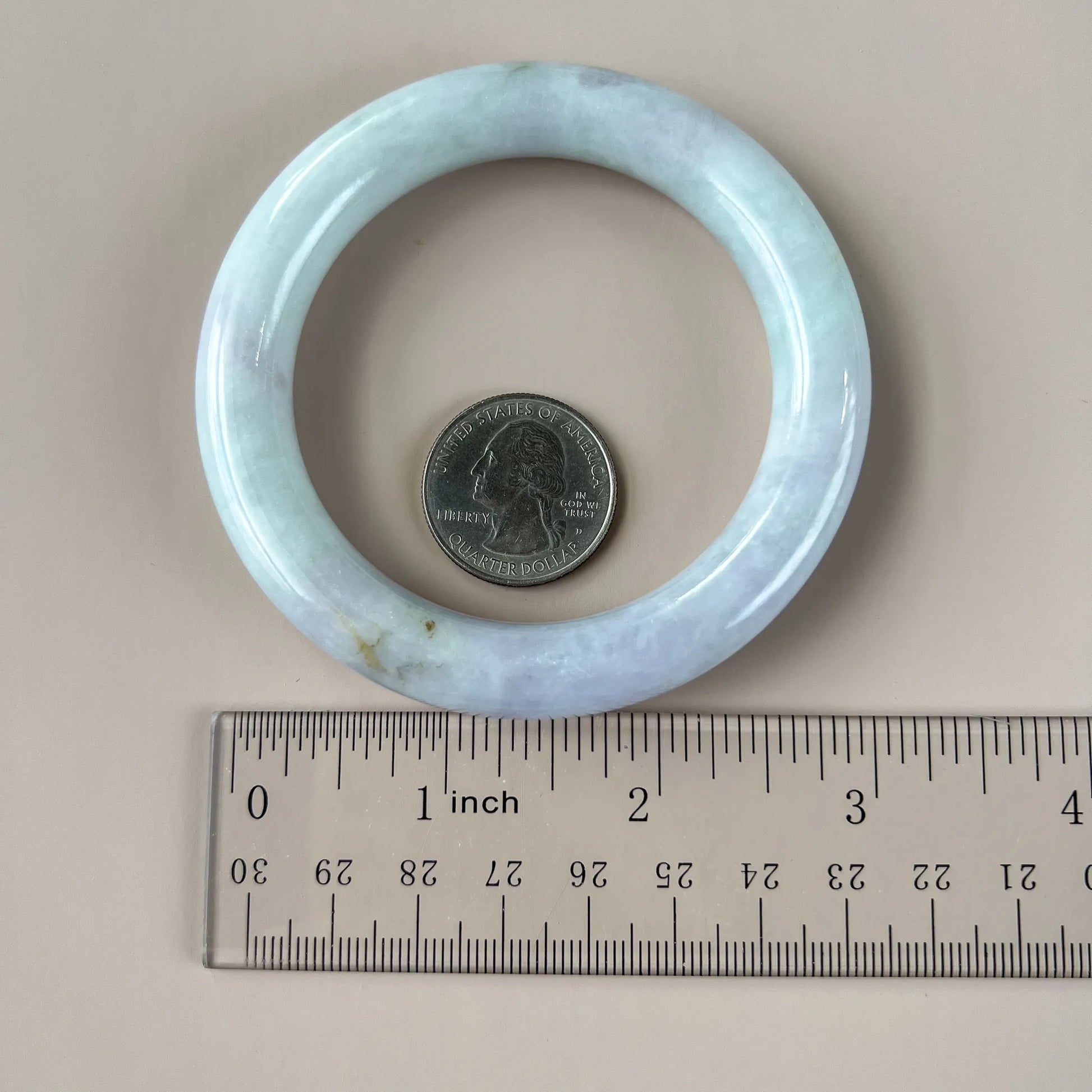 Pale green natural jade bangle shown with ruler and quarter for scale, polished rounded profile