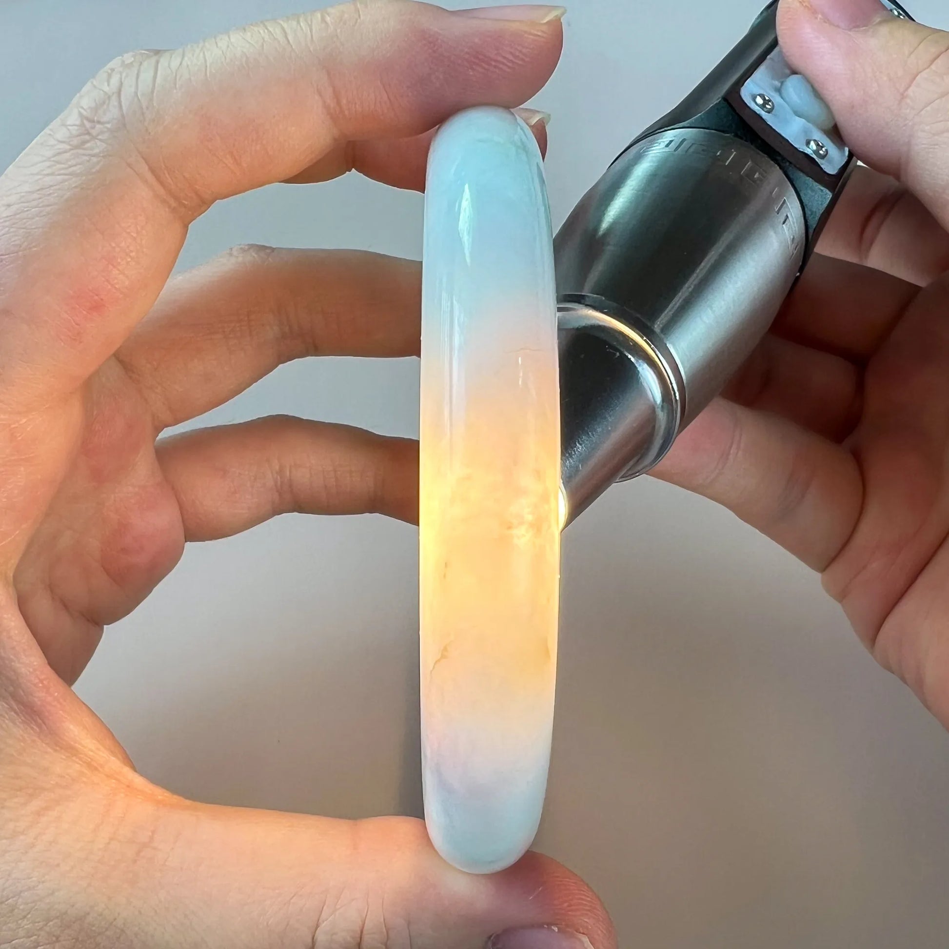 Side view of polished pale blue jade bangle with warm backlighting revealing translucence