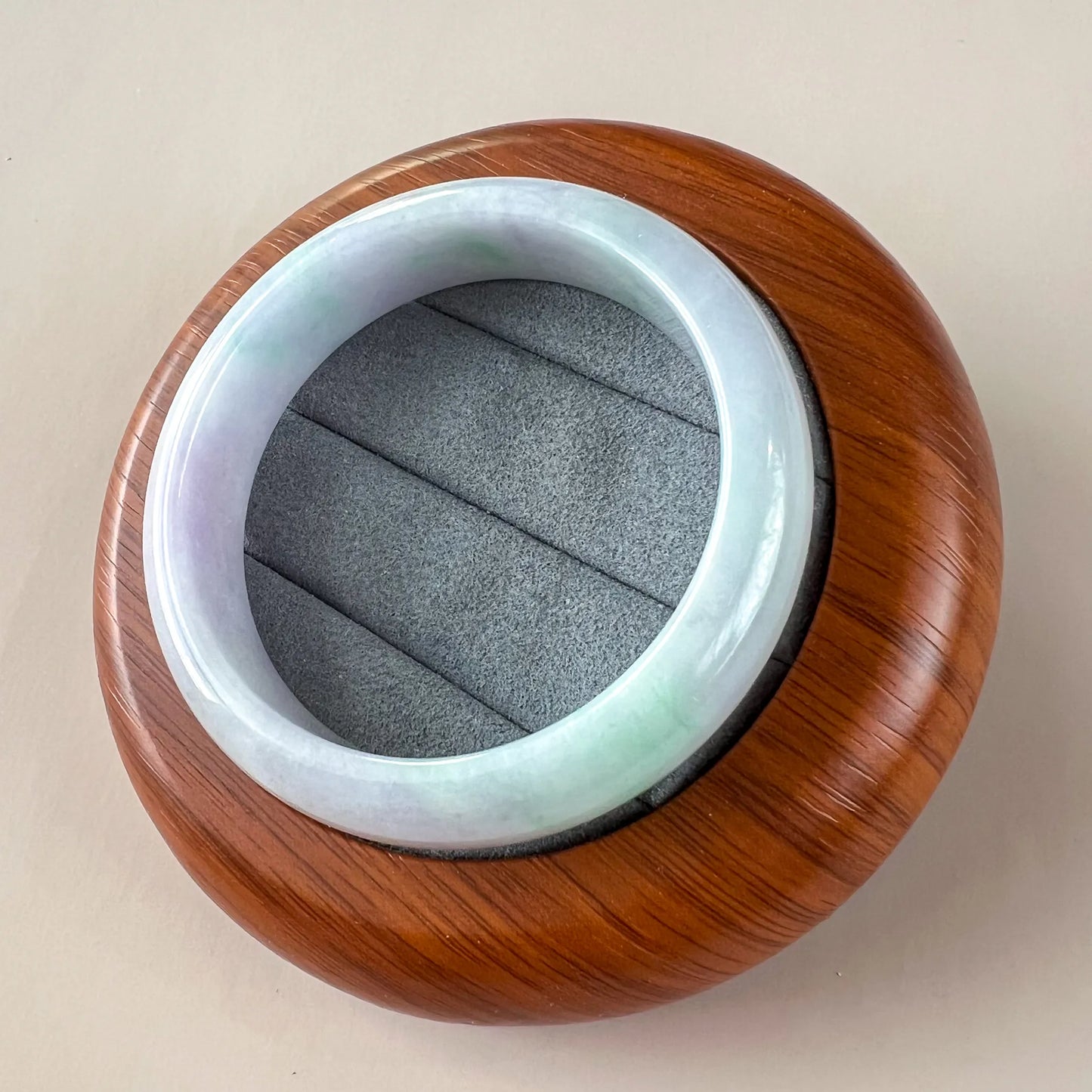 Angled view of smooth jade bangle resting in round wooden display case