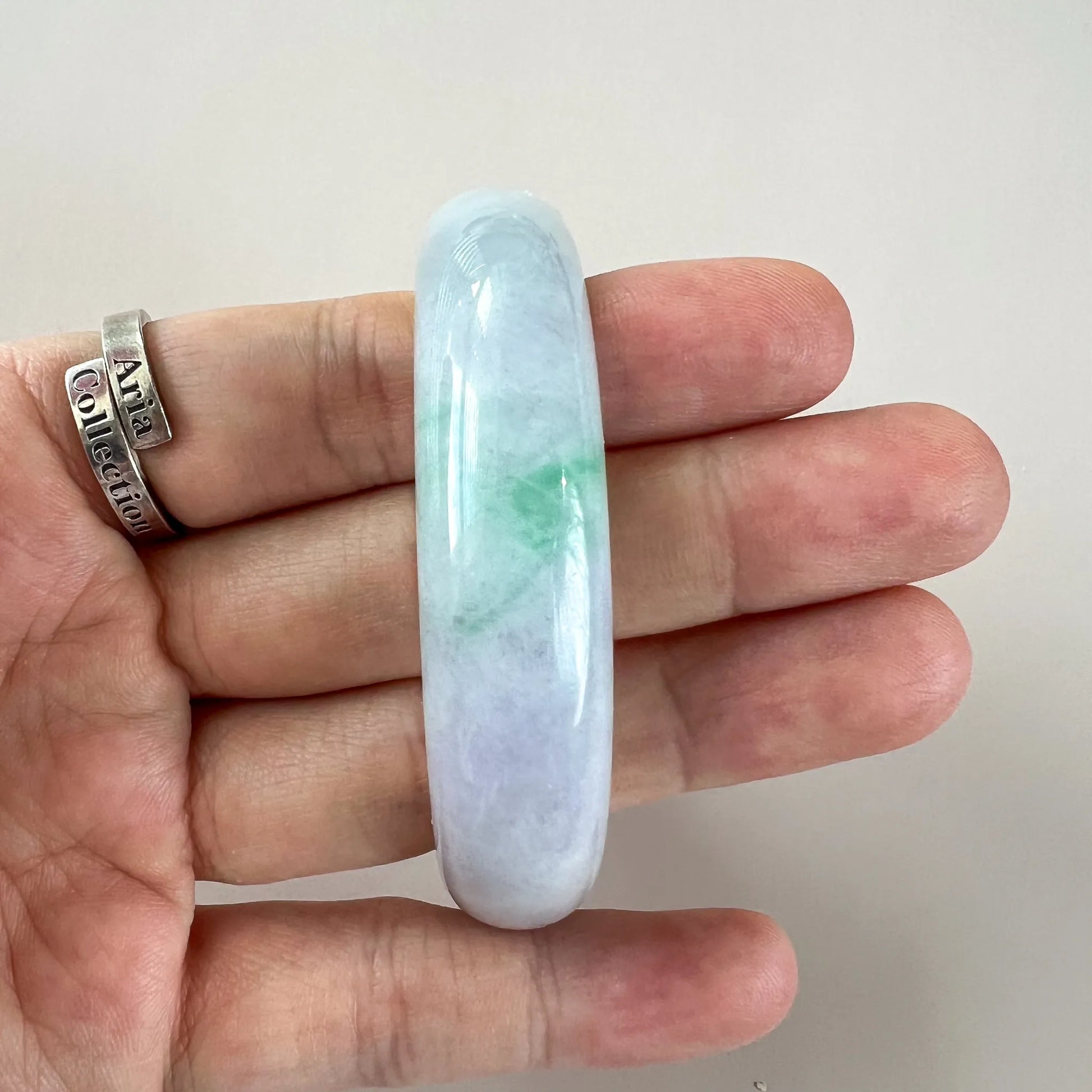 Slim polished jade bangle shown on hand for scale with translucent blue-green tones