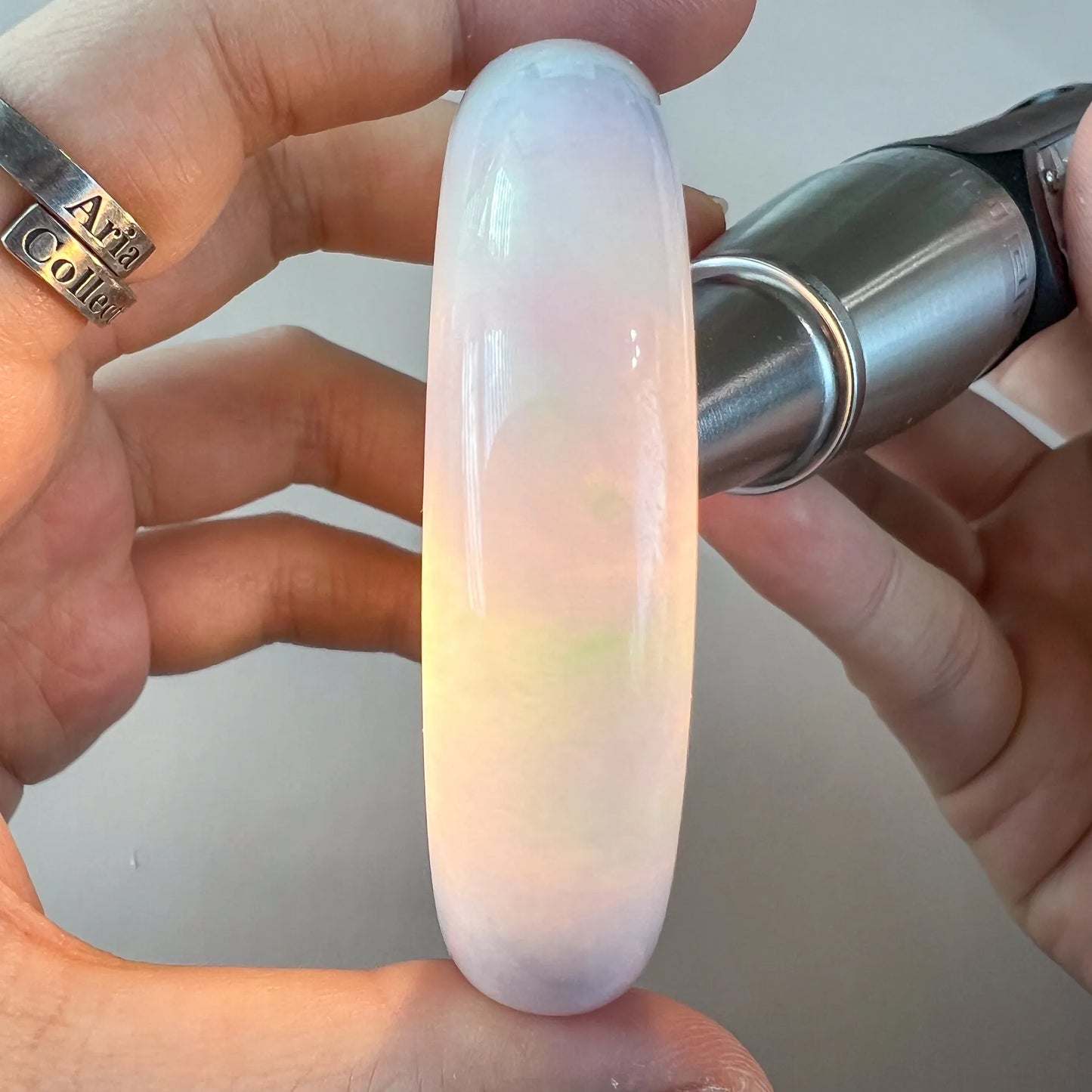 Translucent jade bangle held under light, revealing soft pink and green color zoning