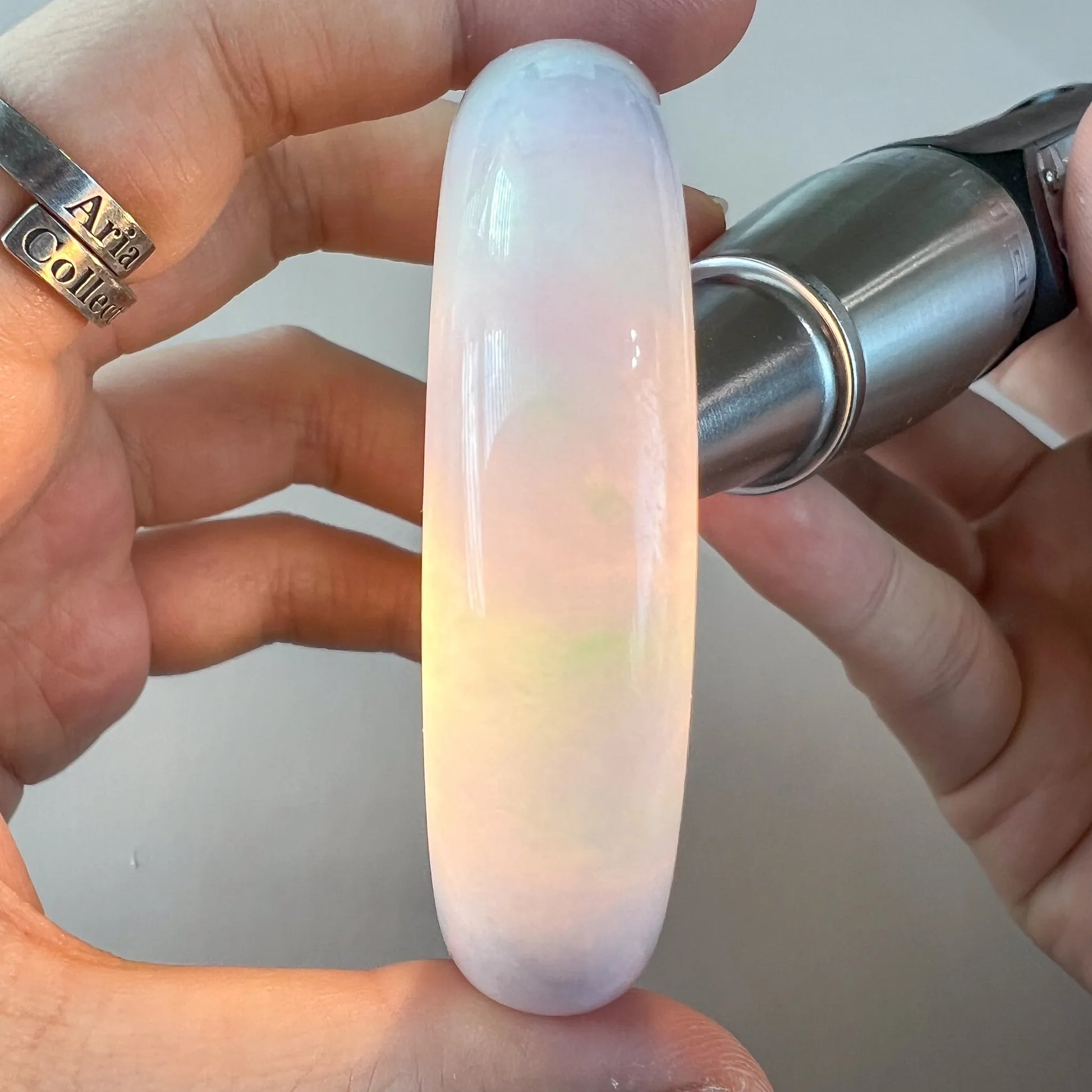 Translucent jade bangle held under light, revealing soft pink and green color zoning