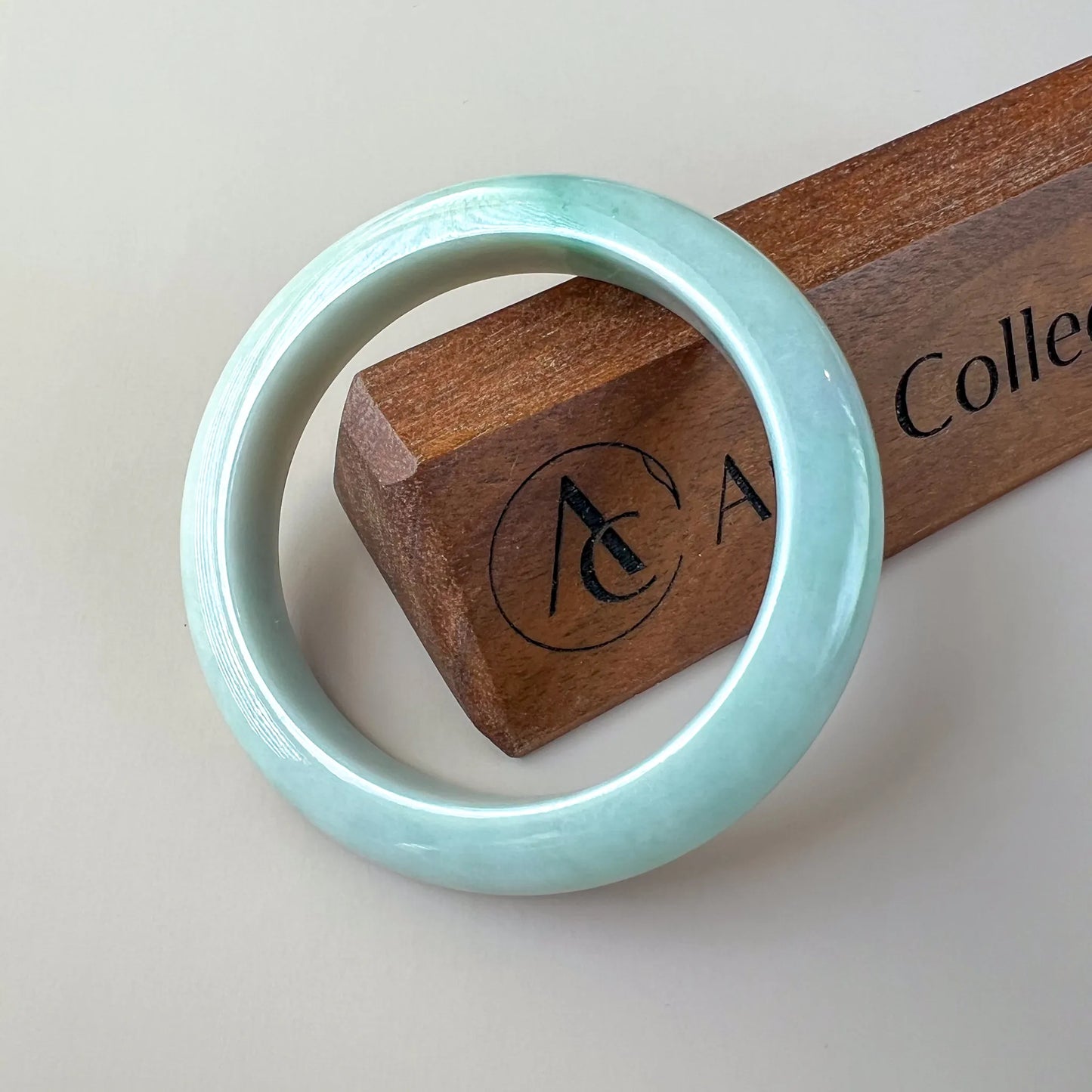 Glossy light blue jade bangle angled on a wooden stand, smooth round profile