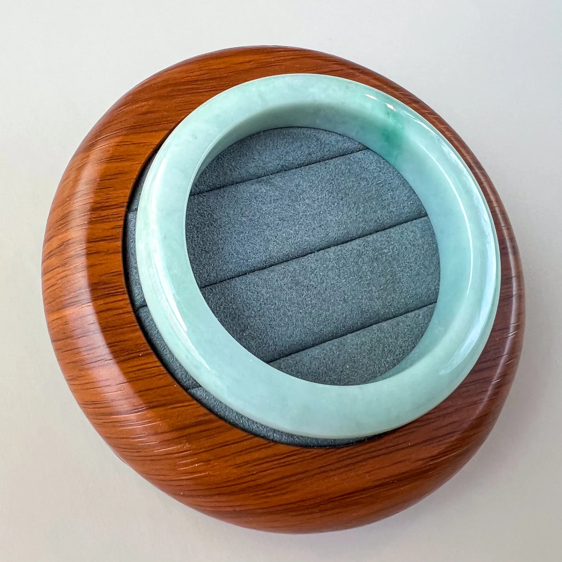Oblique view of smooth pale green jade bangle resting in a round wooden box