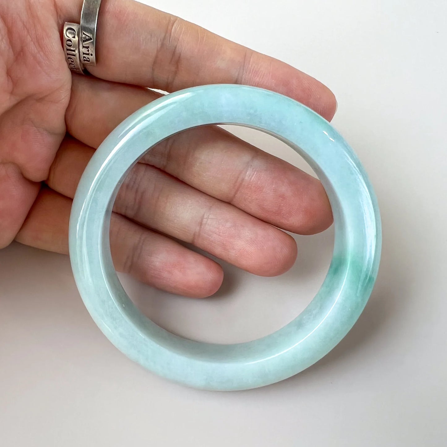 Handheld front view of glossy aqua jade bangle showing size and rounded finish