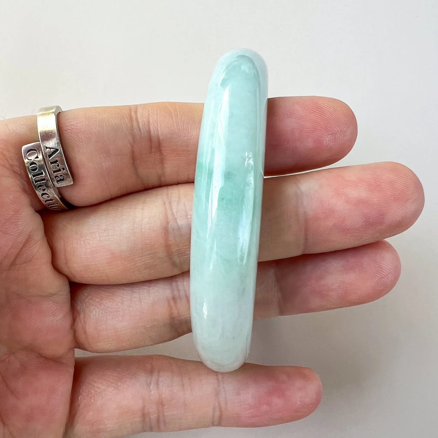 Side profile of polished light green jade bangle held between fingers, smooth finish